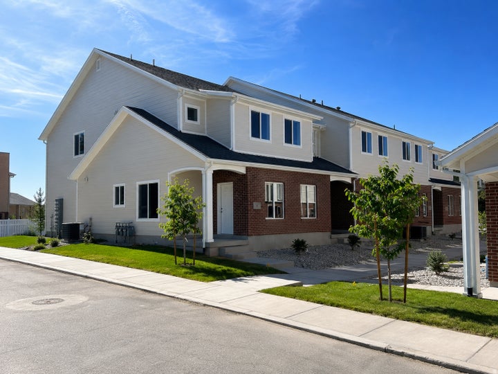 Contemporary townhome exterior featuring brick and light-toned siding, a covered entry, established sidewalks, and newly…