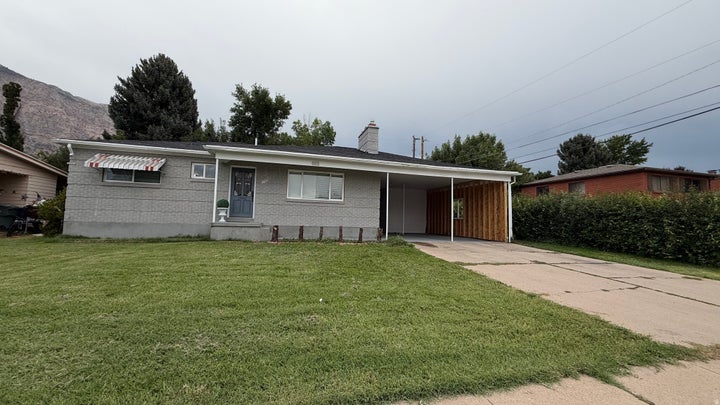 Charming mid-century residence featuring a brick exterior, carport with wood-finish garage door, and expansive front…