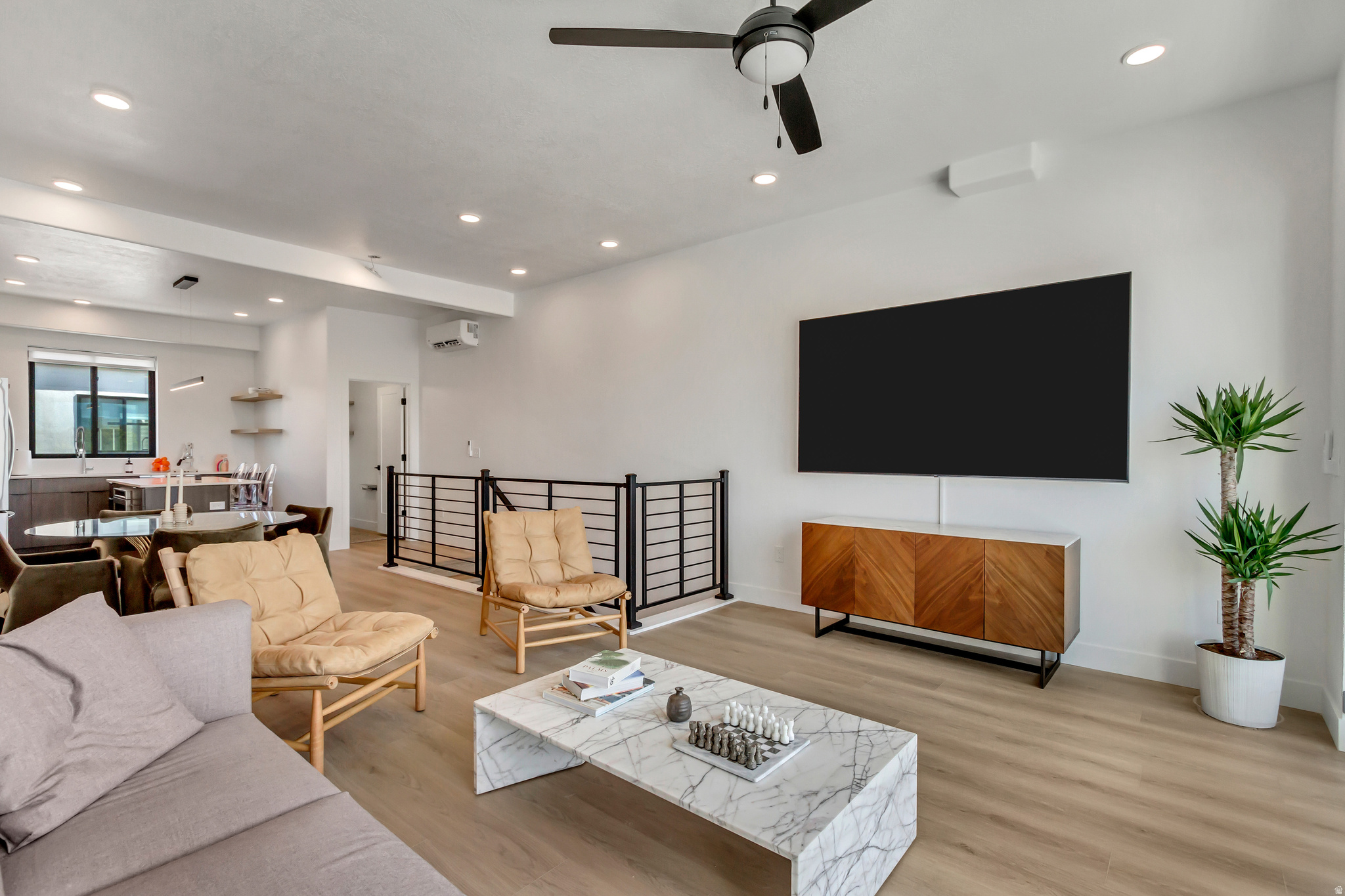 Open-concept living area featuring light wood-finish flooring, recessed lighting, a ceiling fan, and a contemporary black metal railing