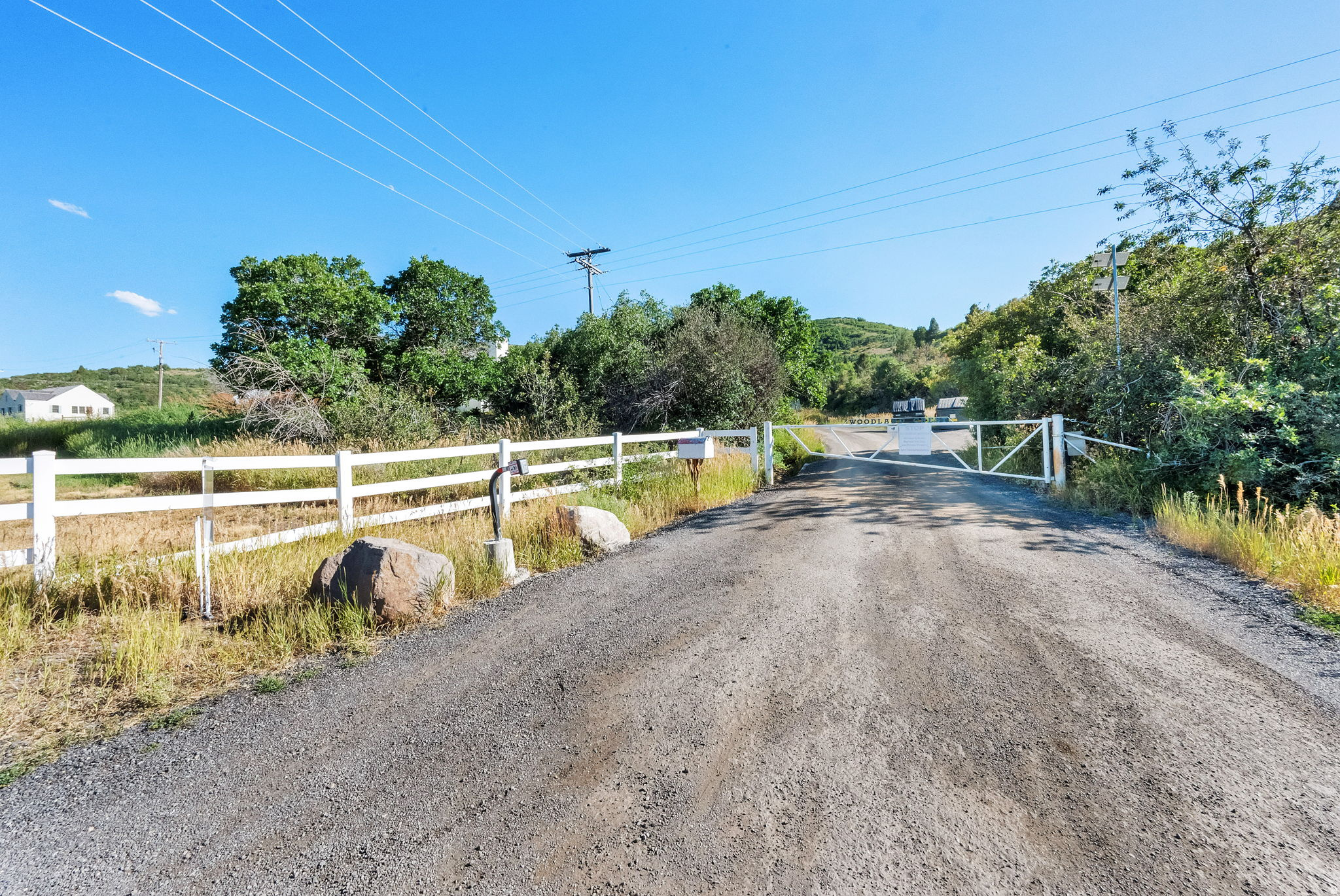 Gravel driveway with a white metal gate, bordered by a white three-rail fence