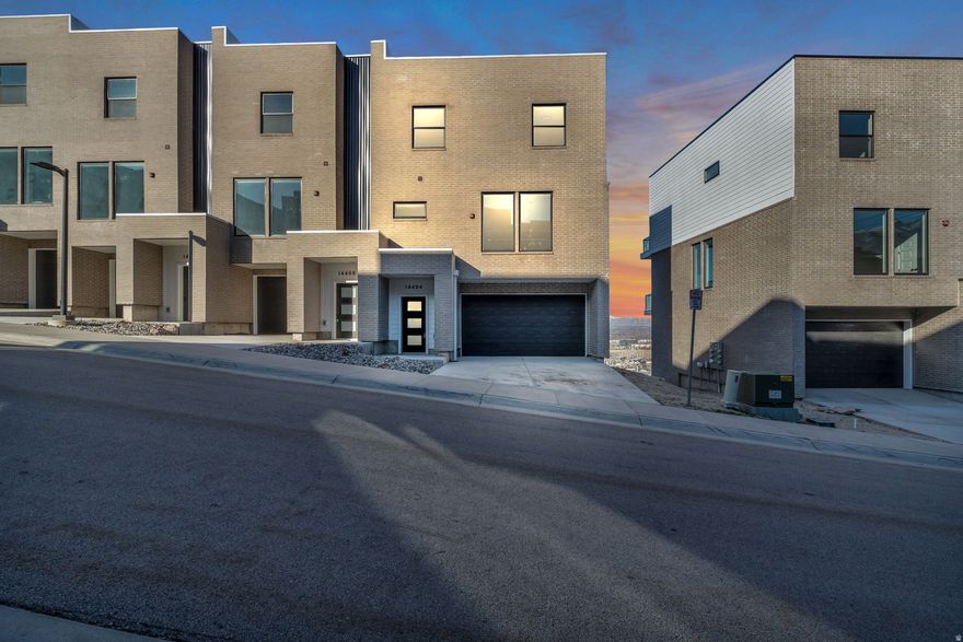 This stunning modern townhome offers sweeping panoramic views from Draper's highly sought-after benches. Ideally located just minutes from I-15, it offers both convenience and a peaceful, elevated setting. The interior is thoughtfully designed with contemporary finishes and an efficient, livable layout. The main level features soaring 10' ceilings, beautiful wood flooring, custom soft-close cabinetry, quartz countertops, striking black windows, and sleek black plumbing fixtures. A tankless water heater and numerous upgrades throughout enhance both comfort and efficiency. Upstairs, three spacious bedrooms include a refined primary suite complete with a private balcony, walk-in closet, and full bath. The lower level offers a versatile bedroom with its own full bathroom and separate entrance -perfect as a guest suite, home office, or additional living space. Loaded with upgrades and showcasing breathtaking valley views, this exceptional townhome delivers modern elegance in one of Draper's most desirable locations.   Square footage figures are provided as a courtesy estimate only. Buyer is advised to obtain an independent measurement.