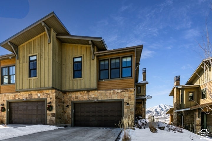 Multi-level residence featuring stone and vertical wood siding, a multi-pane window design, and two attached garage…