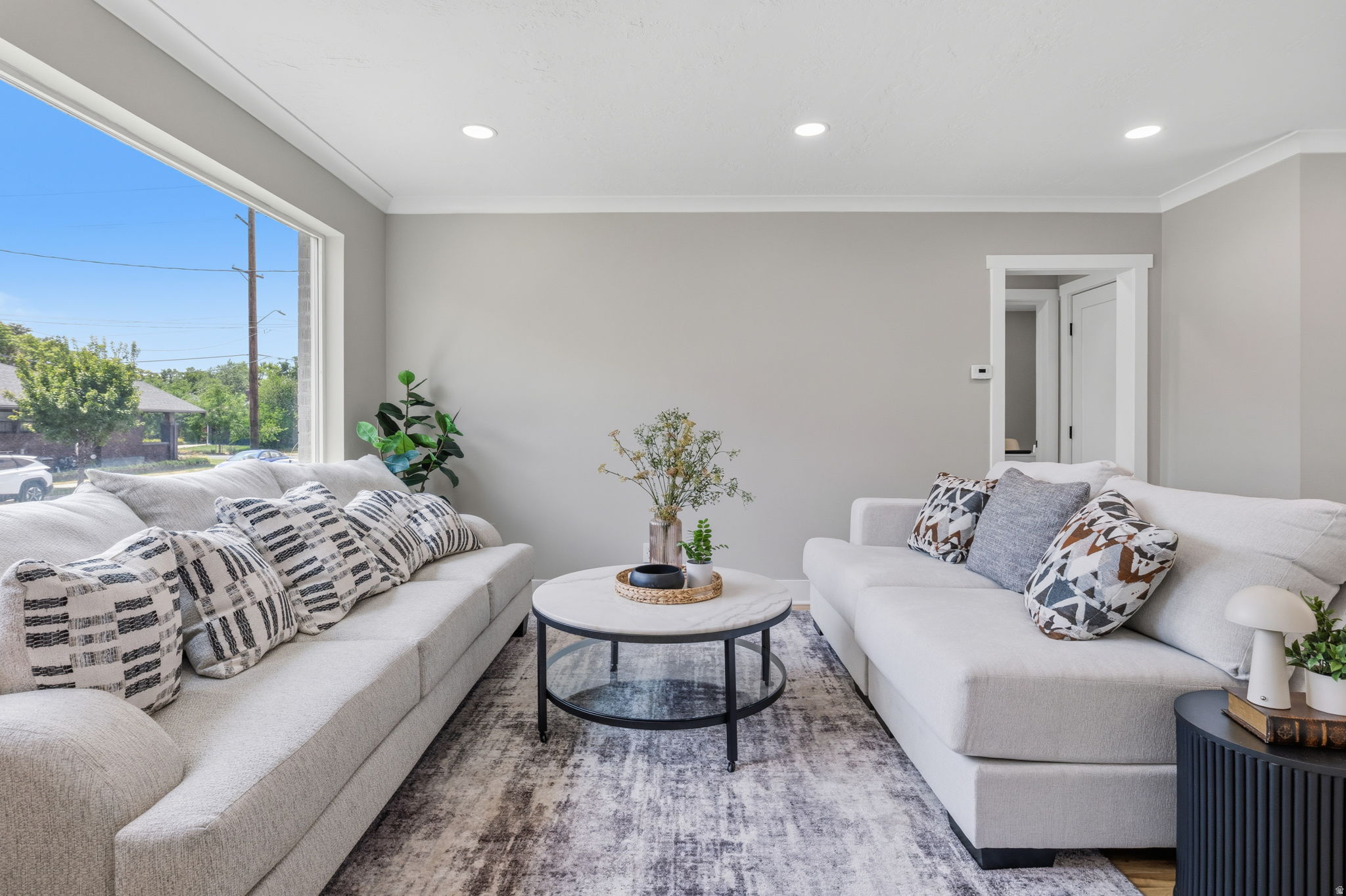 Living area featuring a large picture window, recessed lighting, crown molding, light wood-finish flooring, and a modern aesthetic