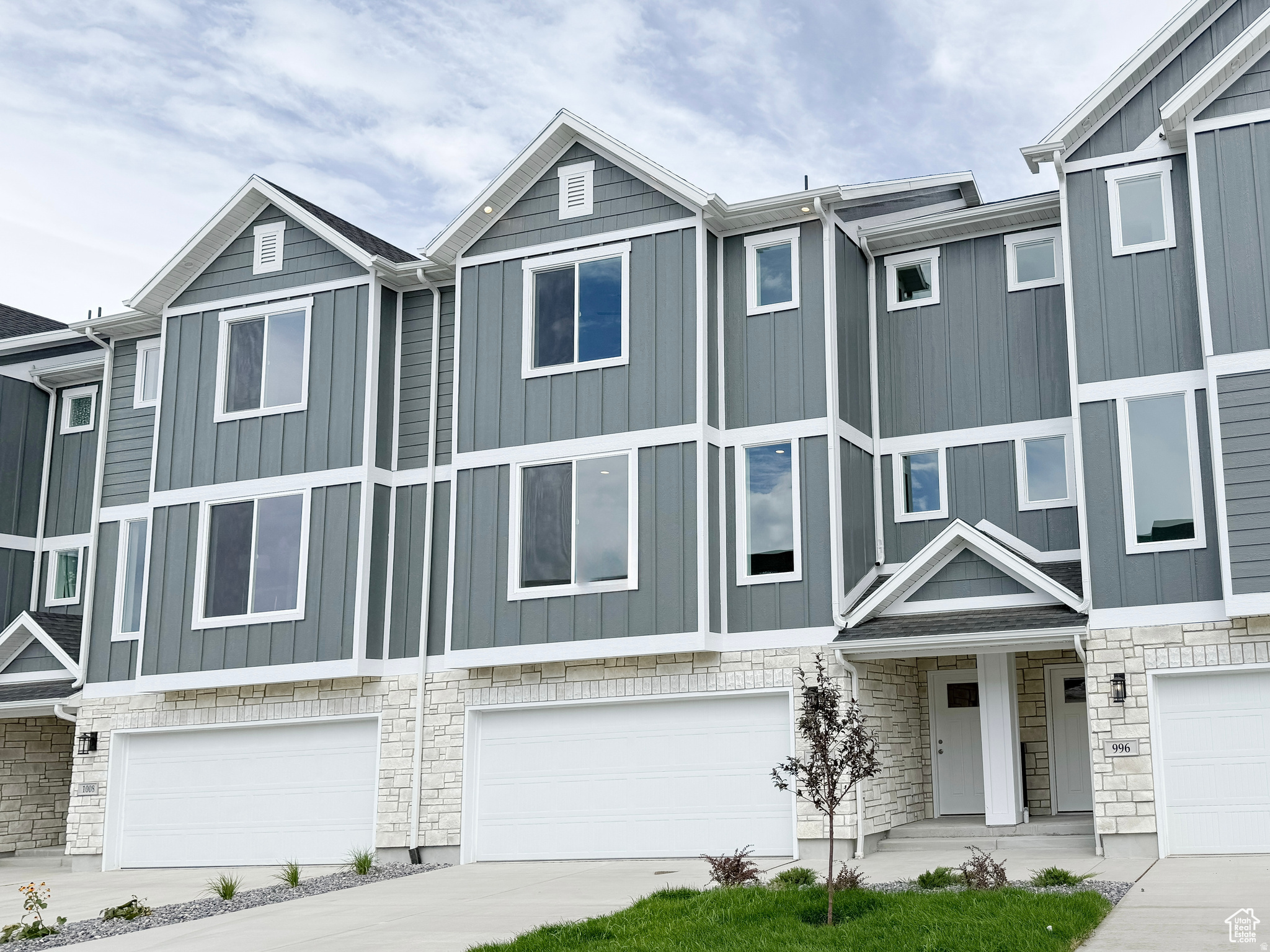 Modern townhome exterior featuring multi-level construction, stone veneer accents, vertical panel siding, white trim, and multiple large windows