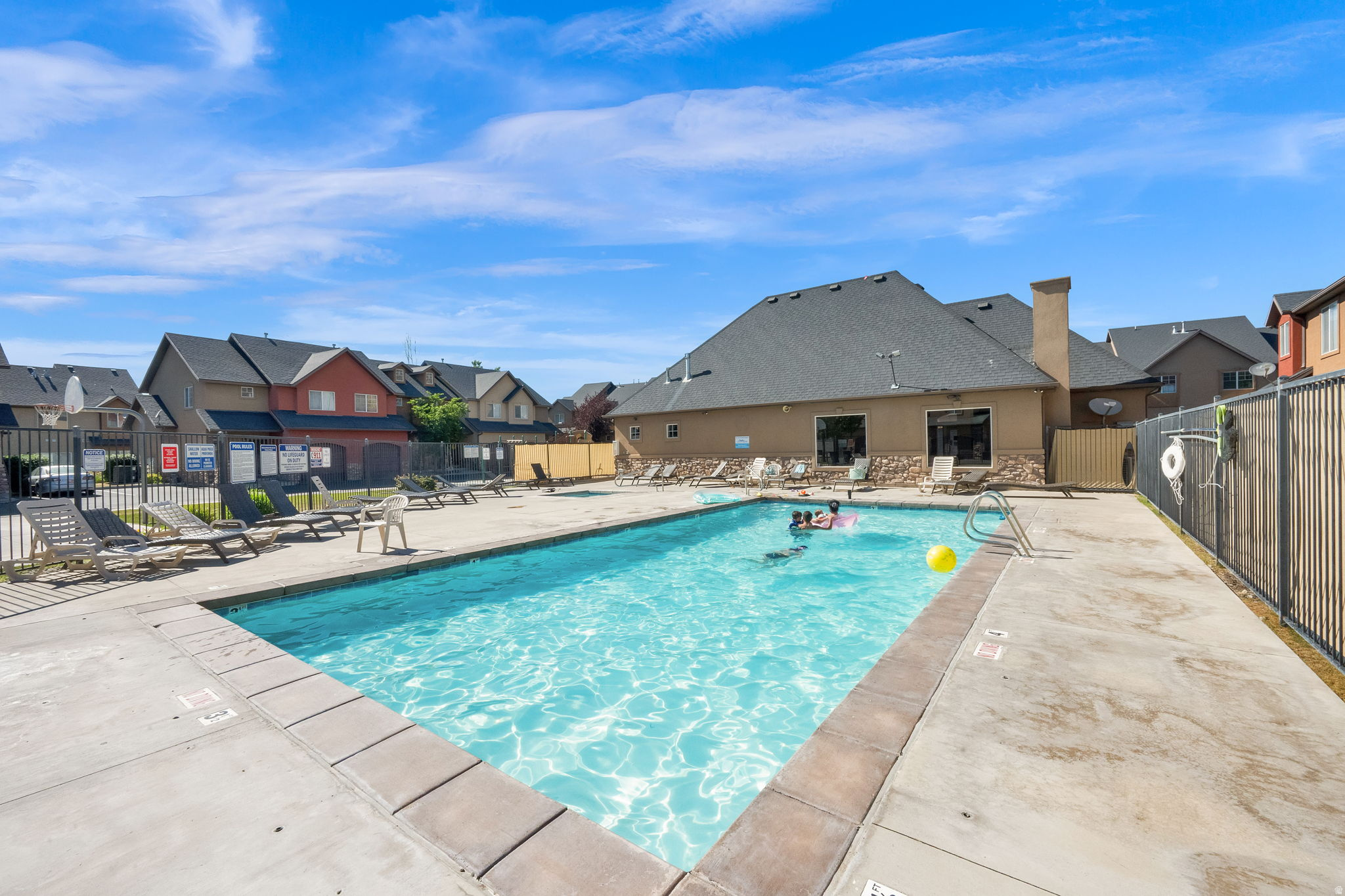 Community swimming pool with concrete decking, surrounding lounge chairs, and a black metal fence