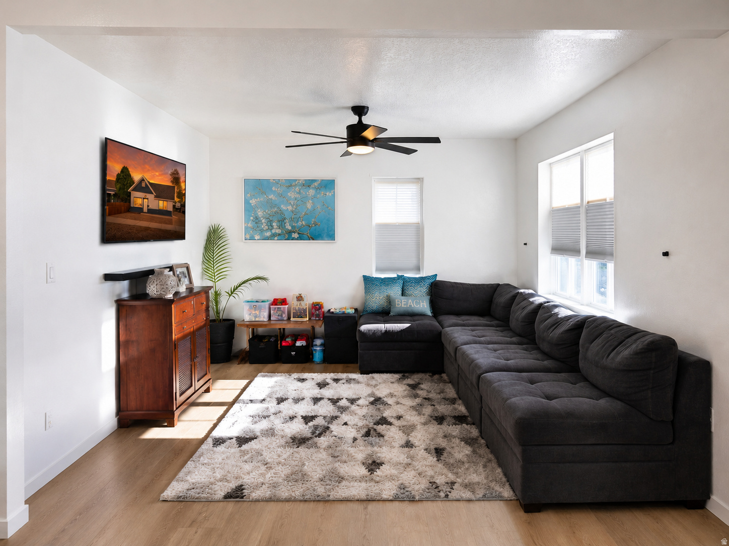 Bright living area featuring wood-finish flooring, white walls, and a ceiling fan with integrated lighting