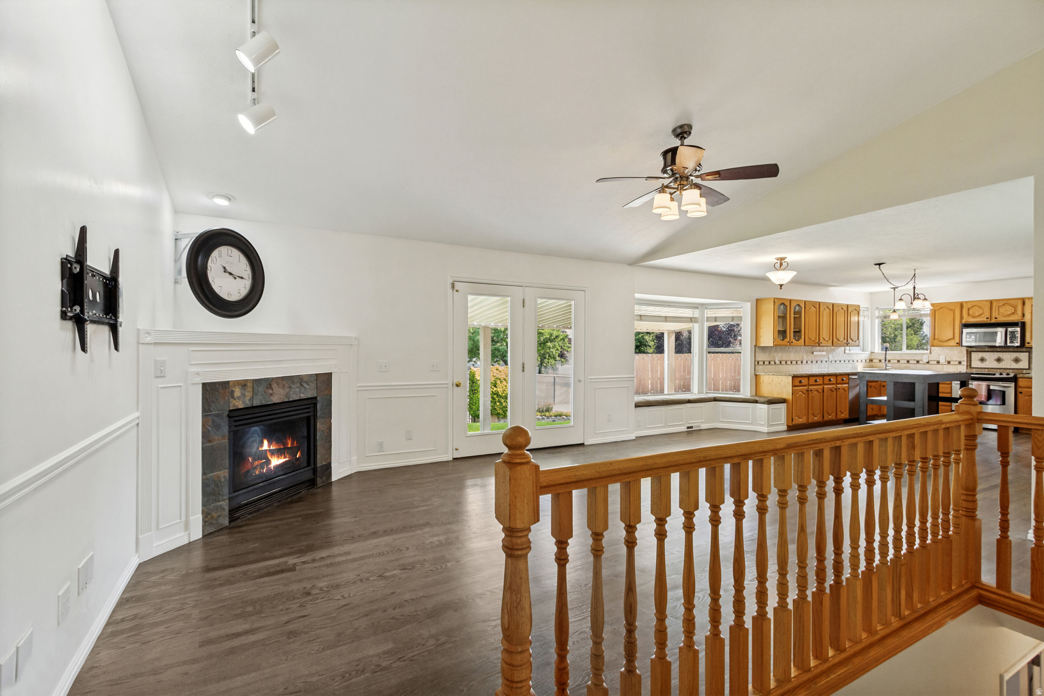 Vaulted ceiling living space featuring a fireplace with stone surround, wood-finish flooring, and French doors