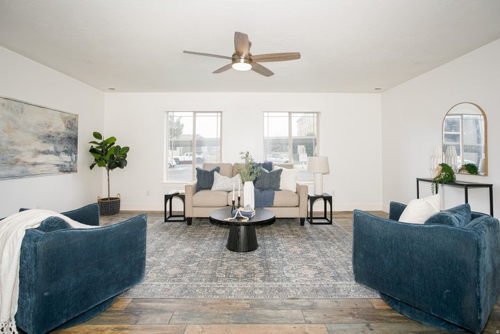Spacious living area featuring neutral walls, wood-finish flooring, a ceiling fan with integrated lighting, and dual…