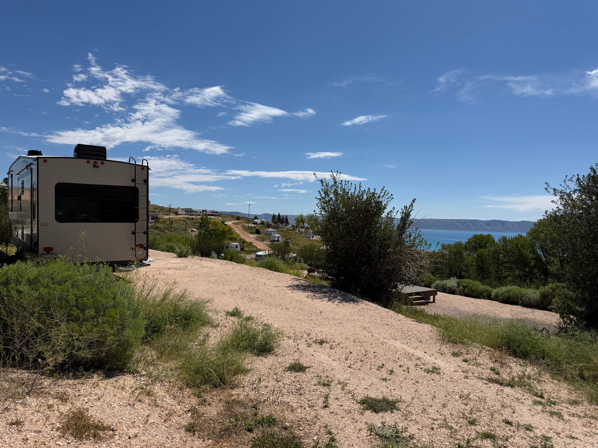 Expansive outdoor space featuring a gravel surface, natural landscaping, and a distant body of water