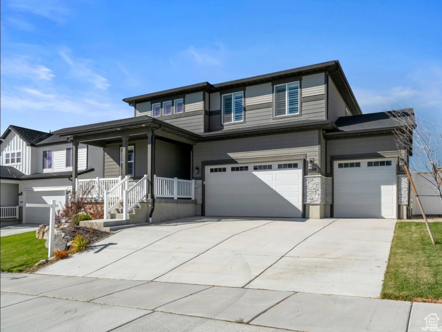 Multi-tone siding exterior featuring a covered front porch with white railings, a multi-car garage, and a concrete driveway
