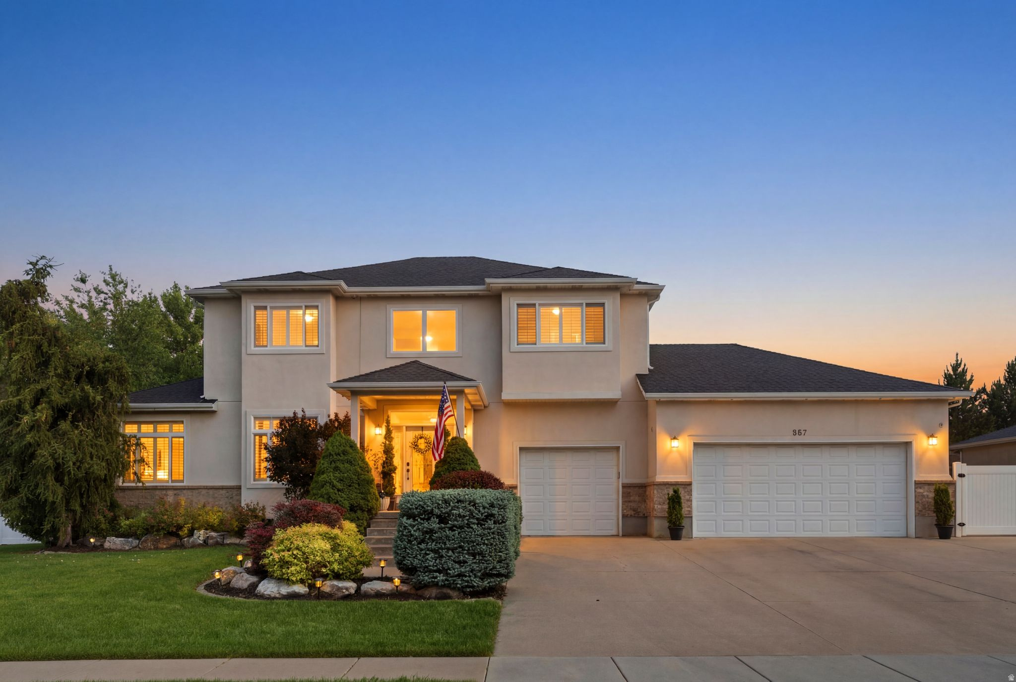 Stucco exterior residence featuring a covered entry, established landscaping, and two integrated garages