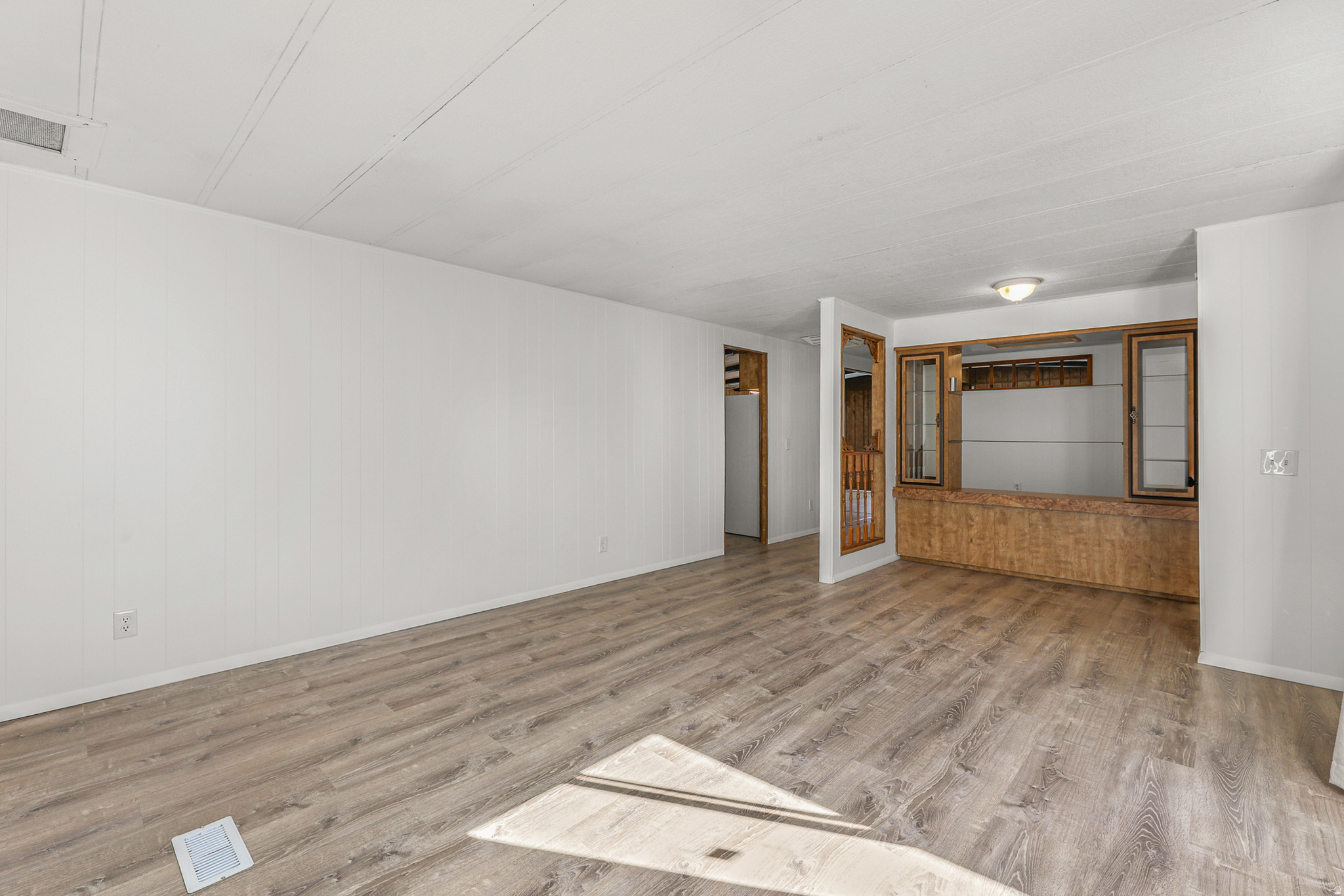 Spacious room featuring wood-finish flooring, white walls, and a built-in display cabinet with glass doors and wood-finish accents