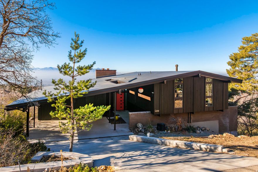 Designed by Glen Ashton Lloyd and built by Research Homes, this Ron Molen residence rests quietly at the end of the road: where the world slows and the architecture speaks. Its classic timber post-and-beam construction, increasingly rare and deeply coveted, anchors the home in both craft and time. The main volume settles confidently behind a privacy wall in front, cool and composed, while the south wing lifts and reaches, cantilevering lightly over the hillside with a butterfly's grace. A stand of scrub oak gathers around the house from the sides and rear, creating a sense of seclusion and belonging. A central walkway leads to the cheerfullyorangefront door, flanked on one side by a carport that is both fetching and befitting. The home's thoughtful siting captures open valley views to the back and preserves privacy from the front. Just steps away, Neff's Canyon Trail offers a direct connection to the woods above and beyond. Inside, the home unfolds through subtle shifts in elevation, with the post-and-beam structure stitching the spaces together. Floating stairs, rough-sawn timber walls, sunken conversation areas, and Molen's signature bedroom built-ins reveal a deep understanding of how people live, gather, and retreat. This is a home shaped around movement, between indoors and out, between shared moments and quiet pauses. Intentional, expressive, and deeply human -- this isquintessentialMolen.
