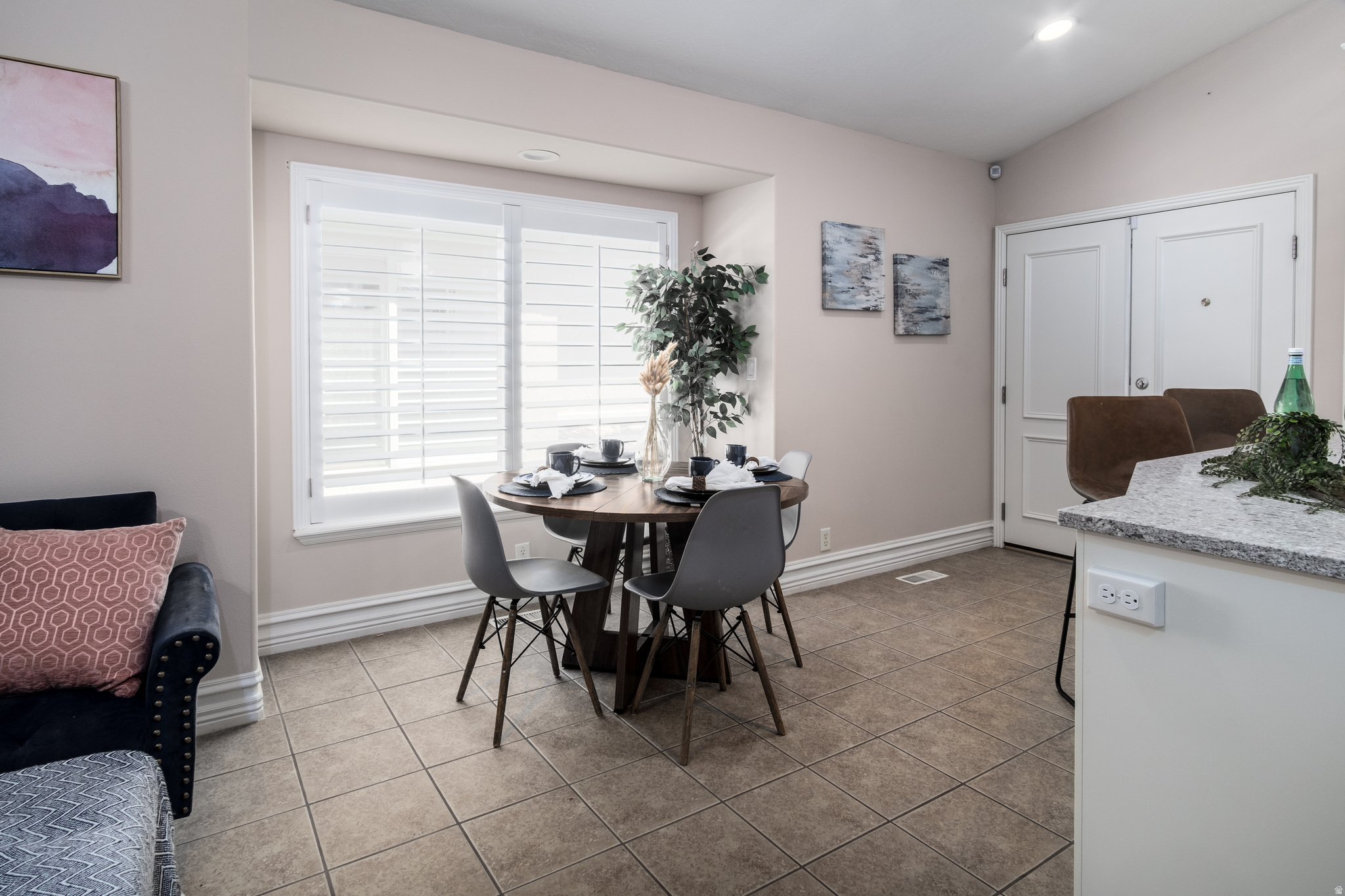 Dining area with ceramic tile flooring, a window featuring white plantation shutters, and a vaulted ceiling