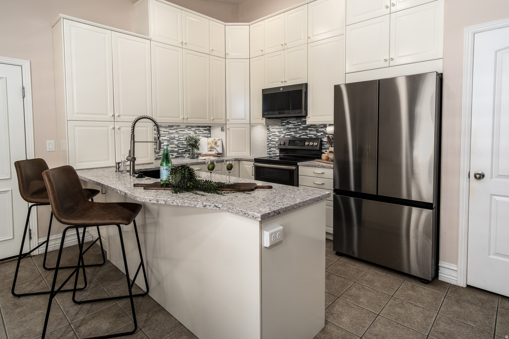 Kitchen featuring an island with a light-toned countertop, white cabinetry with upper storage, a stainless steel refrigerator, a black range, and a patterned backsplash
