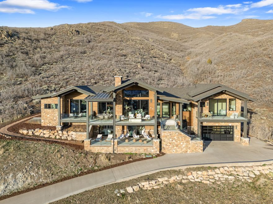 Welcome to one of the best views overlooking Park City-you'll feel like you're living at a retreat every day, with stunning views of Deer Valley, Lake Jordanelle, and Mt. Timpanogos. Enjoy private outdoor living designed to restore the body, quiet the mind, and reconnect you with nature.  Located on a private cul-de-sac and backing to hundreds of acres of pristine land, this extraordinary 5,112-square-foot, 4-bedroom plus office residence offers rare privacy, epic views, and serenity.  Summer living shines here, with multiple outdoor spaces to relax and gather. The private back patio features a sunken hot tub overlooking the ravine and a sauna. A short hike from your backyard leads to even higher vantage points for unforgettable sunsets.  The home was intentionally designed to move in rhythm with nature. Morning light fills the open living area from the east, while expansive windows frame breathtaking sunsets to the west. A striking limestone fireplace anchors the space, complemented by crystal double countertops and wood-clad ceilings that add warmth and texture throughout the main level.  The primary suite captures both sunrise and sunset, supporting a natural sleep cycle. The spa-like bathroom features dual vanities, a double-headed shower with Deer Valley views, and a European handcrafted clay soaking tub.  Each guest bedroom includes a private ensuite and outdoor access, offering comfort and privacy. A second living space downstairs opens to a covered deck with swinging chairs-perfect for taking in the expansive views.  Designed for visual calm and flow, the home features recessed door framing, no baseboards, and soft limewash walls throughout, including the showers.  The Sanctuary is more than a home-it's a place to breathe, reset, and experience peaceful living just 10 minutes from Park City.
