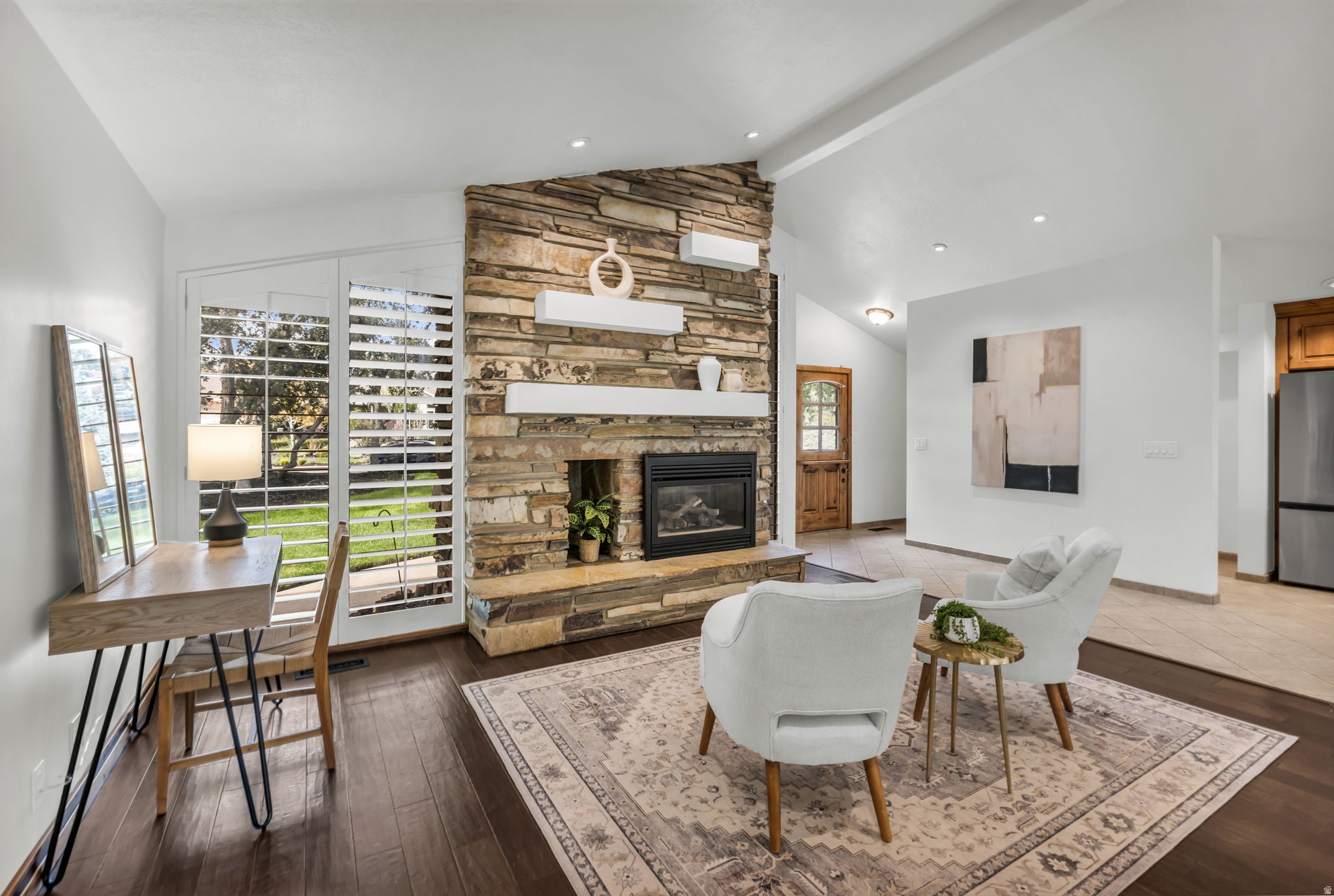 Stone-clad fireplace with built-in shelving, dark wood-finish flooring, white plantation shutters, vaulted ceiling, and recessed lighting