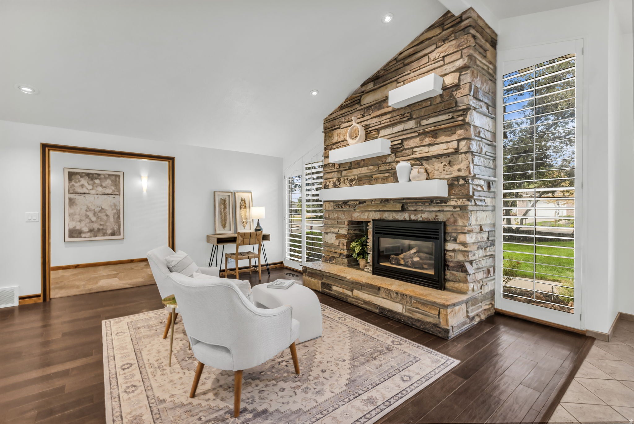 Stone-faced fireplace with hearth, vaulted ceiling, wood-finish flooring, recessed lighting, and plantation shutters