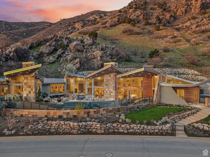 Welcome to a once-in-a-lifetime architectural masterpiece at the mouth of Big Cottonwood Canyon. Designed by acclaimed architect Guy Dreier, this 9907 sq ft estate is a stunning fusion of modern design and the raw beauty of nature. Set on a dramatic mountainside lot just across the canyon from Post Malone's residence, this home is as visually striking as it is unforgettable.  With a sweeping roofline that evokes the elegance of vast sails, the architecture soars-inside and out. Floor-to-ceiling glass walls fully retract to reveal an infinity pool, a cascading waterfall that flows beneath a glass-floor hallway, and a cliffside hot tub just off the primary suite. Every element is designed to blur the line between indoors and out.  The home has been completely reimagined with the finest materials. Nearly $1,400,000 in recent upgrades have been invested throughout the home, elevating both form and function with the finest materials and attention to detail. The chef's kitchen is a showpiece of both function and style. A full guest suite downstairs offers comfort and privacy, and the unfinished second basement is the perfect setting for a future home theater. The south wing is structurally engineered to support a second story-unlocking unobstructed 180-degree views of the entire Salt Lake Valley.  The expansive lot stretches up the mountain with space to add a second guest house or retreat. This is more than a home-it's a landmark of inspired living.