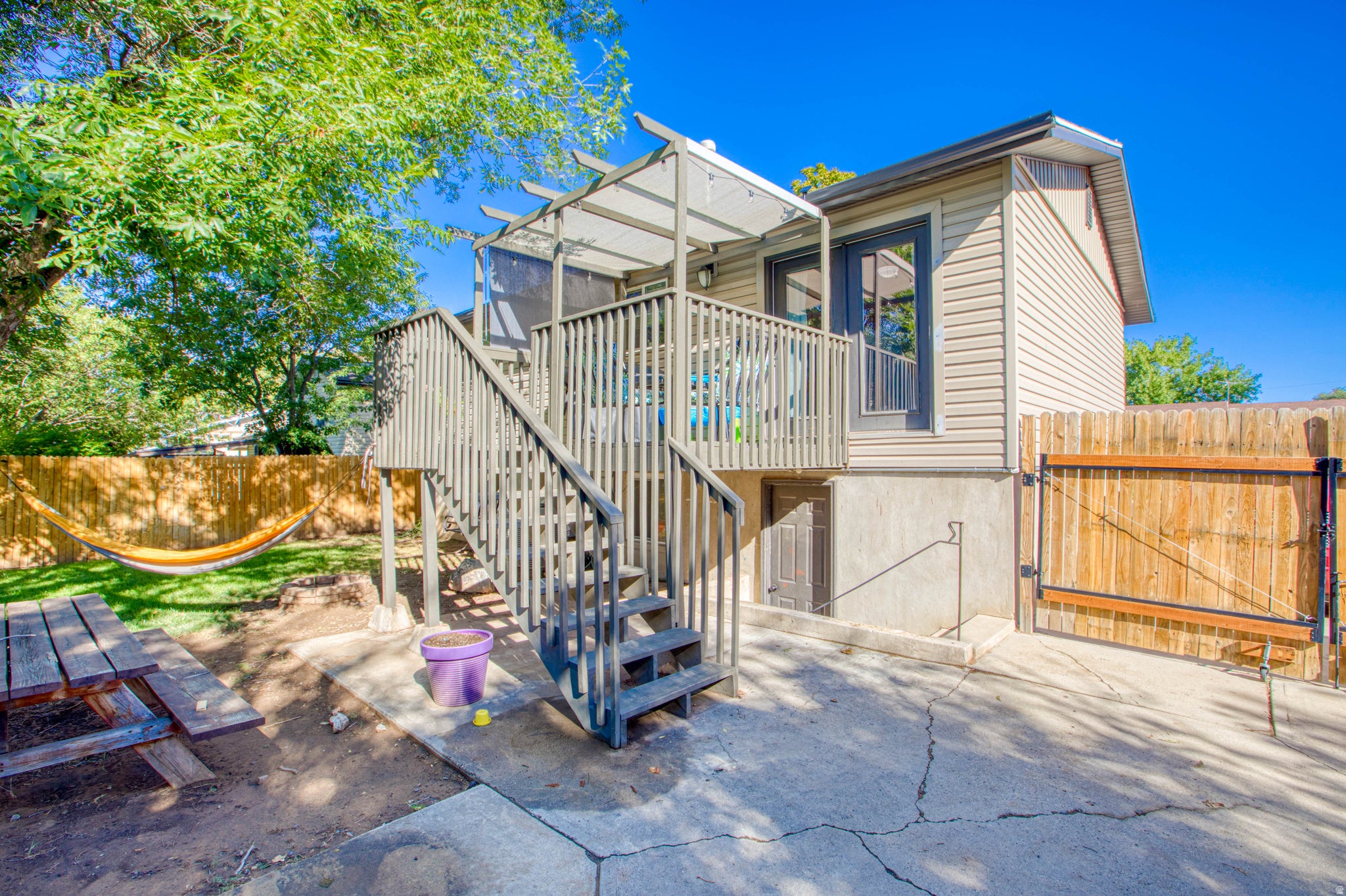 Elevated deck with pergola, exterior door access, wood privacy fencing, concrete patio, and mature trees