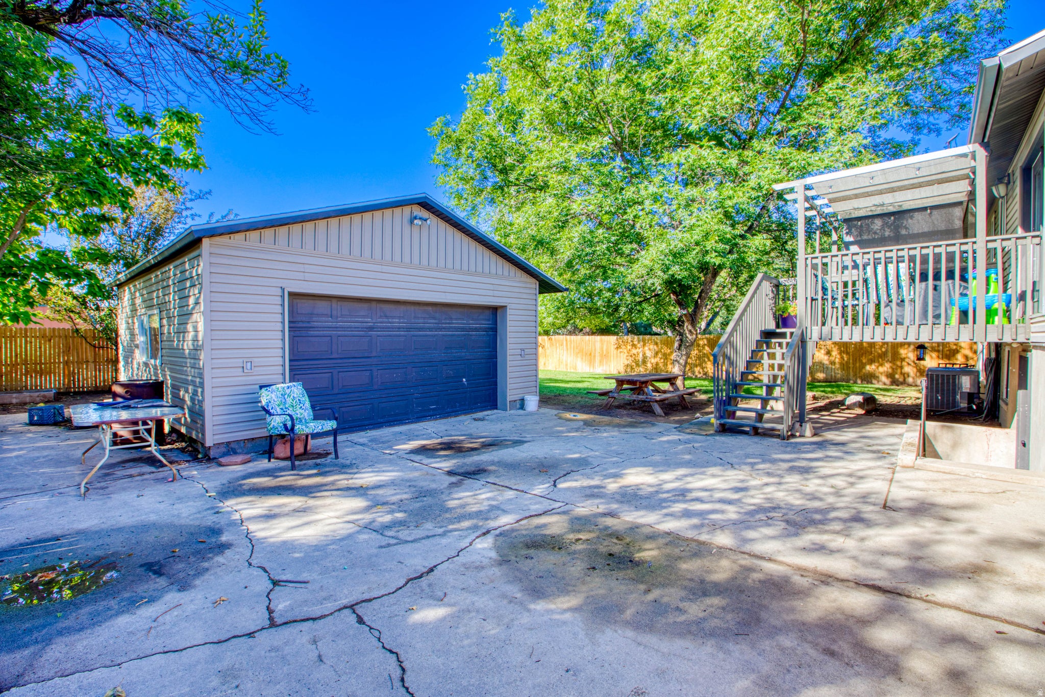 Detached garage with a roll-up door, spacious concrete patio, wood deck with stairs, and a fenced perimeter
