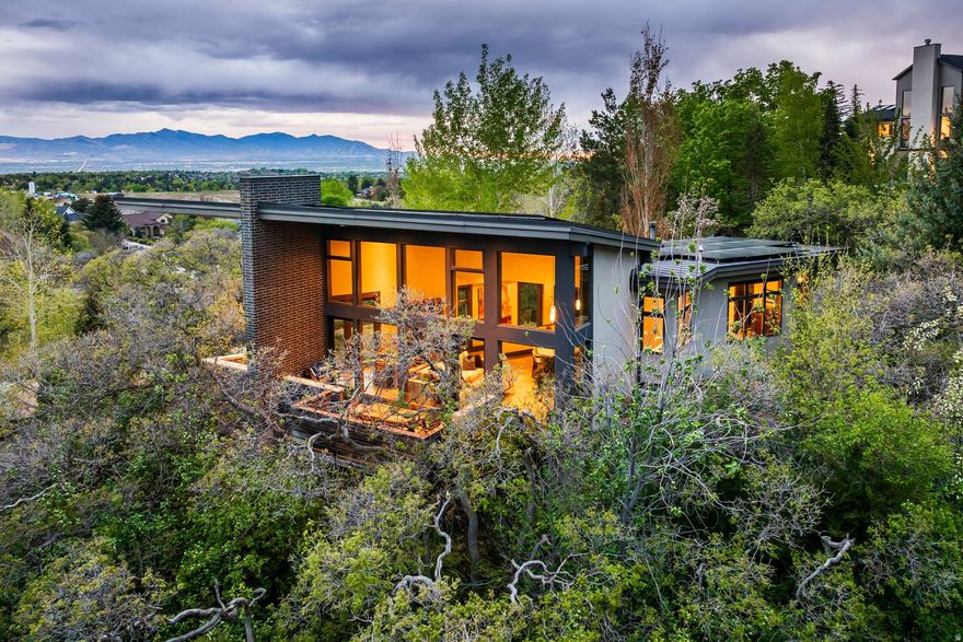 Introducing a one-of-a-kind, custom-built home featuring spectacular mountain views and massive windows looking directly up into Little Cottonwood Canyon. Ideally located just outside the mouth of the canyon, this contemporary retreat perfectly balances high-end architecture with mountain functionality. The home's centerpiece is a breathtaking 32-foot wide, 17-foot high wall of glass that frames panoramic views of the rugged peaks. Whether you are seeking a high-performance full-time residence or a world-class mountain getaway, this property offers a rare combination of quality craftsmanship and sustainable living.  Property Highlights: The View: Dramatic floor-to-ceiling windows looking directly up Little Cottonwood Canyon. Energy Independent: 43 owned solar panels on the roof, upgraded electrical panel, and a Tesla EV charger in the 2-car garage. Artisan Finishes: Imported granite floor tiles, solid hardwood doors and trim, and a chef's kitchen with Sub-Zero, Wolf, and Asko appliances. Outdoor Living: 0.25-acre lot, professionally landscaped with boulders and mature trees, featuring a 40-foot stone terrace and private hot tub