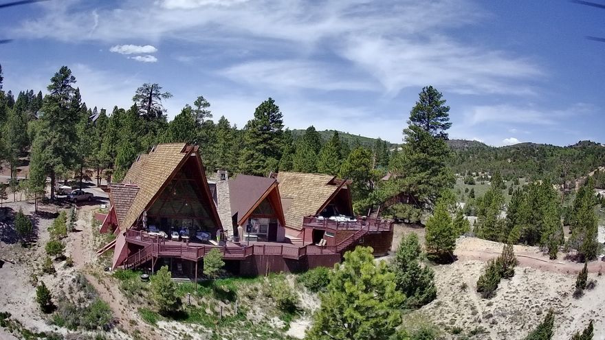 This unique 7000+ square foot, triple A-frame cabin on 9+ acres with mature pines and a large meadow, is located off Hwy 89 at LongValley Junction, midway between Bryce and Zion National Parks in Southern Utah. The nine acres are composed of three lots, one on each side of the cabin, one of which has a full septic system installed. Power and water are connected. The property features 9 bedrooms, 5 full baths, 1 half bath, 2 full kitchens, three family rooms, three propane furnaces, two 1,000 gallon leased propane tanks, three wood burning fireplaces, 20 KV Generac whole house generator, two laundry rooms, two car garage, game room, spa, Hobbit Hut, parking for 10+ vehicles, four RV hook ups with power and EV charging station.