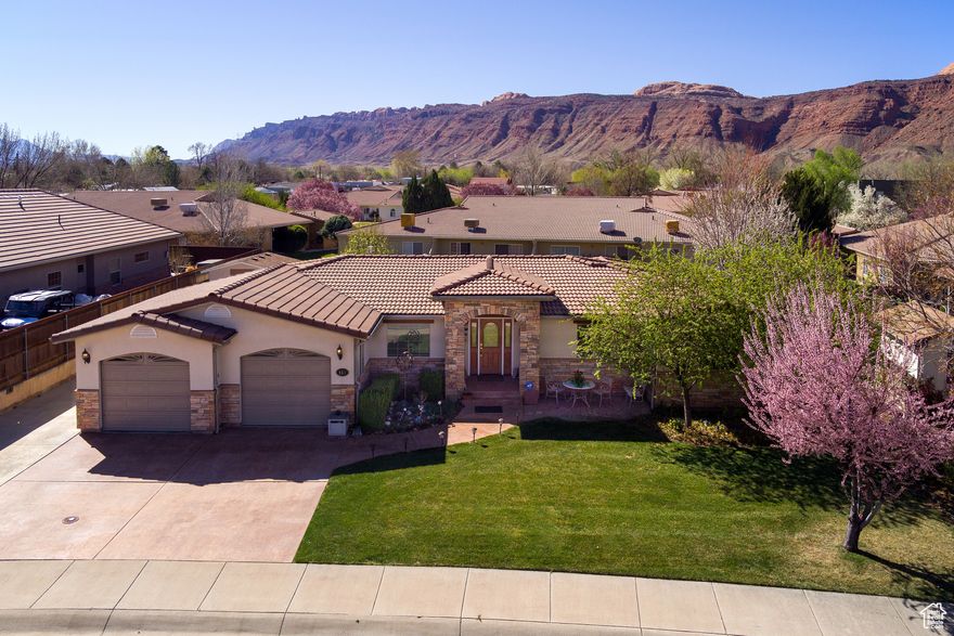 EXCELLENT DEAL ON this beautiful 3-bedroom, 3-bath Mediterranean home which offers nearly 2,000 sq. ft. of one-level living in a peaceful, sought-after Moab neighborhood. Enjoy easy access to parks, schools, churches, and quick entry/exit to bike trails leading into Moab's stunning red rock country.  The home's striking exterior features a 12-foot stone entryway, enhancing its beautiful curb appeal. Inside, a spacious foyer with cherry wood floors flows into the dining room and kitchen. Custom cherry wood columns lead you into the great room, an ideal space for both entertaining and relaxing by the fireplace.  The chef's kitchen is equipped with beautiful white and gold appliances and rich cherry cabinetry that complement the hardwood floors. Adjacent to the kitchen, the cozy family room opens to a private stamped concrete patio, surrounded by vibrant flower gardens and mature cherry and pear trees-perfect for outdoor living.  The Primary bedroom suite offers a tranquil retreat with a spacious walk-in closet, direct patio access, and a luxurious en-suite bath with dual sinks. Designed with energy efficiency in mind, the home features double-pane low-E windows, a 50-year concrete tile roof, refrigerated air, forced air gas heat, and an energy-efficient furnace.  Additional features include an oversized 2-car garage with ample storage, extra parking along the east side for your Moab toys or RV, and a matching stucco shed with an oversized door for larger items.  This well designed home blends elegance, comfort, and practicality in one of Moab's most desirable locations. All information is deemed reliable by listing office; buyer to verify all.