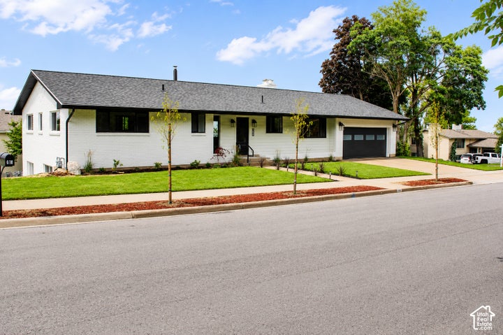 Contemporary ranch-style home featuring white brick exterior, black-framed windows, dark gray garage door, and…