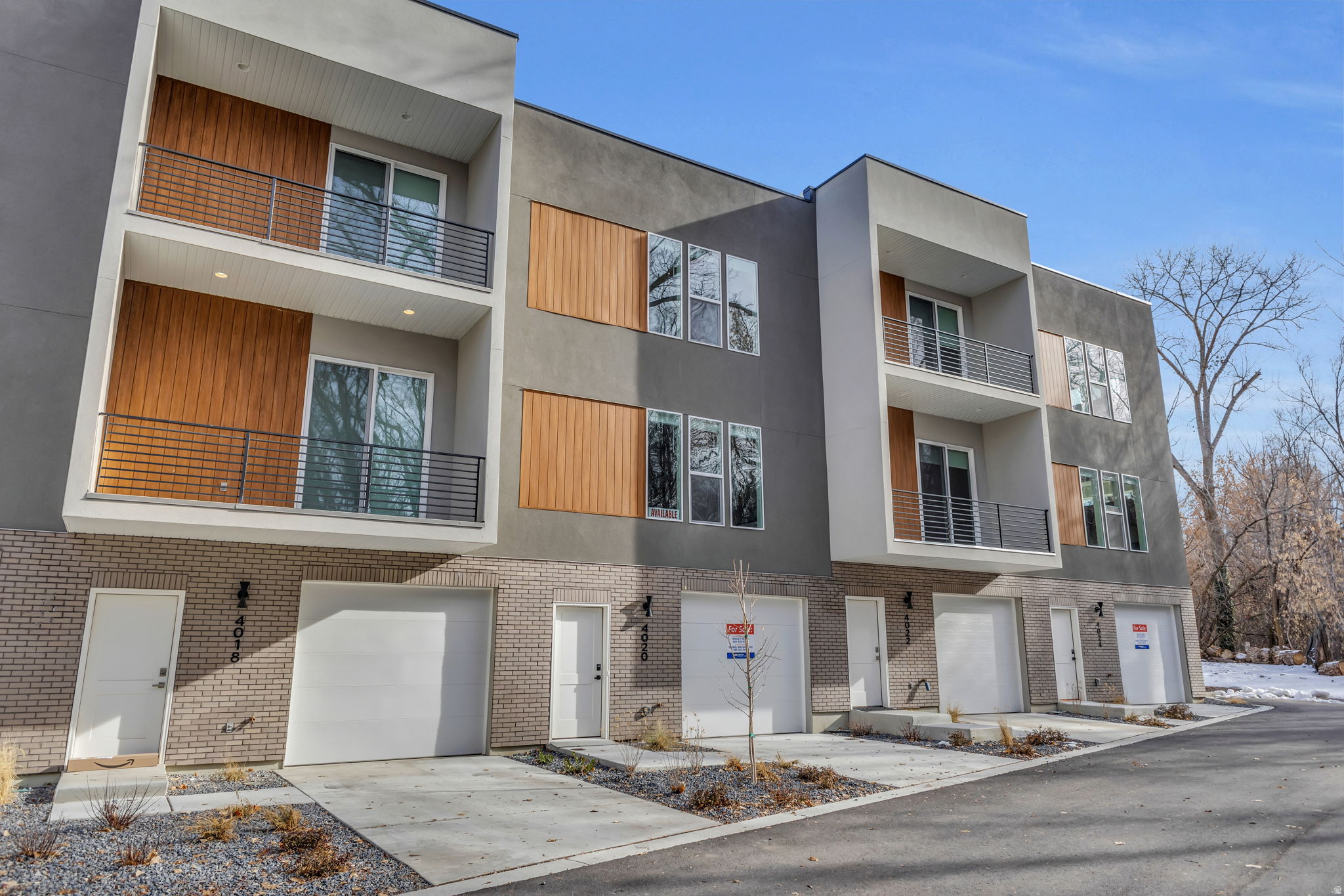 Contemporary townhome exterior featuring multi-level balconies with metal railings, a light brick facade, wood-finish panel accents, and integrated garage doors
