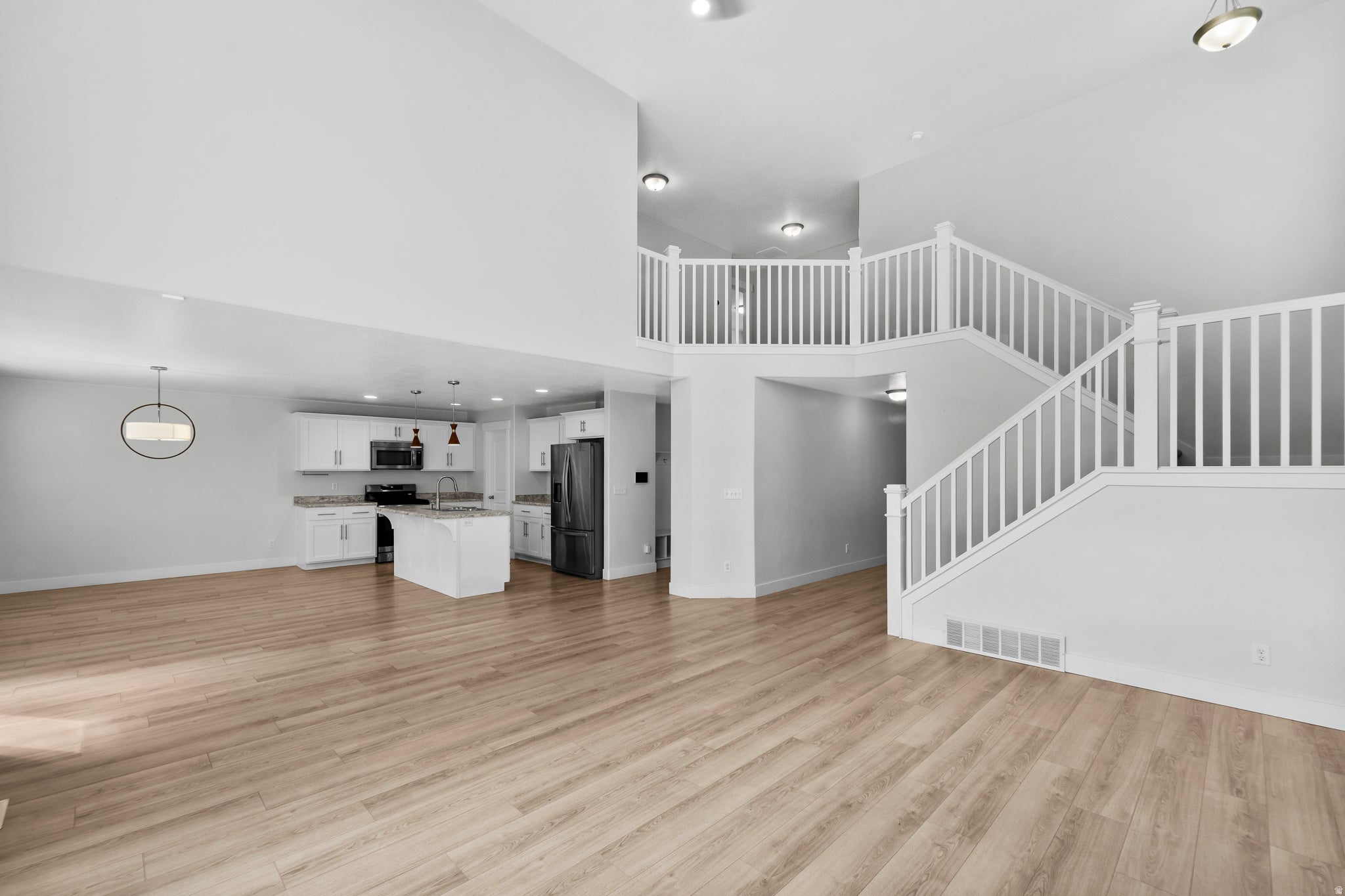 Breathtaking open living area defined by elegant vaulted ceilings that create dramatic architectural interest and abundant natural light. An upper-level balcony overlooks the space, adding dimension and visual flow between levels. Light wood-finish floori