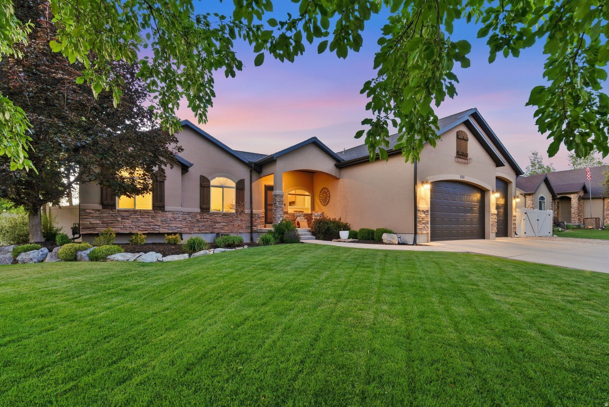 Stucco and stone facade with arched windows, dark wood shutters, and an attached two-car garage