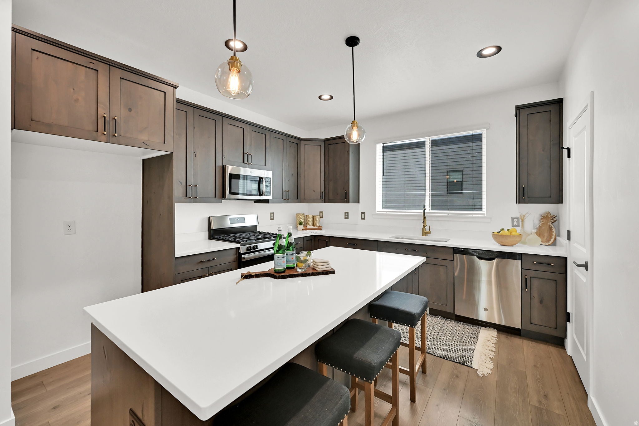 Kitchen featuring a white countertop island, wood-finish flooring, stainless steel appliances, dark wood cabinetry, and recessed lighting
