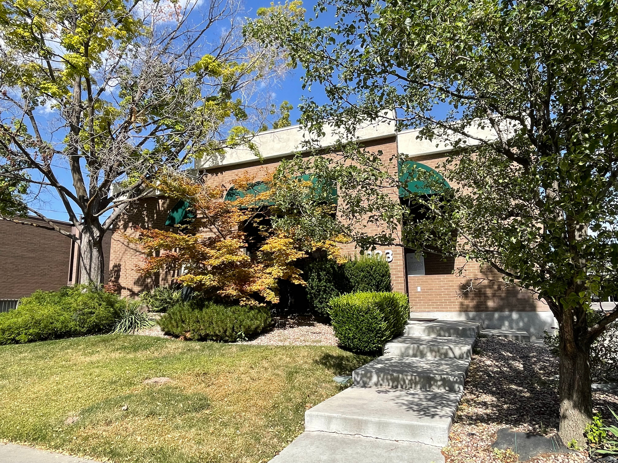 Brick facade building with arched green awnings, mature trees, and a concrete pathway