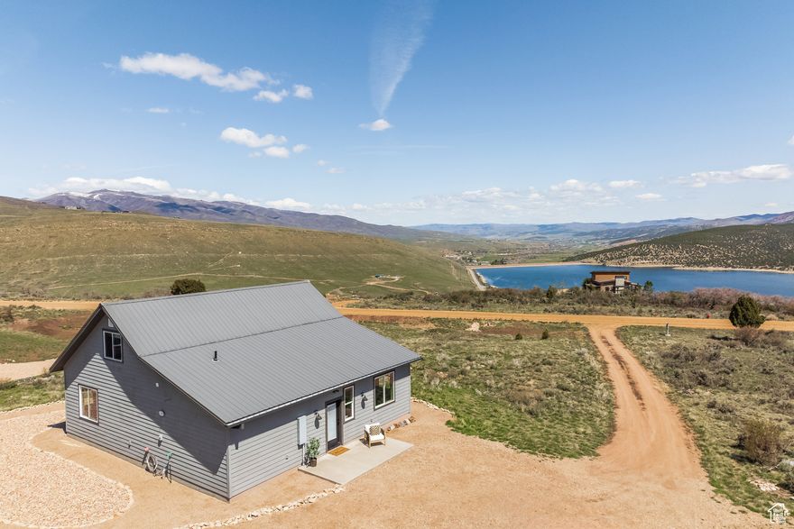 Tucked within the private gates of Lake Rockport Estates, this elevated mountain retreat pairs serene luxury with panoramic lake views. Sited on a rare, flat one-acre lot, the residence offers both seclusion and expansive sightlines over Rockport Reservoir. Inside, a bright, open-concept layout is anchored by granite countertops, solid wood cabinetry, and stainless steel appliances-an ideal backdrop for intimate gatherings or post-lake unwinding. Expansive windows flood the interior with natural light and frame breathtaking vistas, while a gently sloped driveway ensures effortless access year-round. The design seamlessly fuses rustic textures with modern amenities, creating a warm yet refined living experience. Recently completed professional rock landscaping introduces a sculptural, low-maintenance exterior-perfectly suited for all-season enjoyment. Whether savoring morning coffee on the patio, gathering beneath a starlit sky, or embracing quiet moments surrounded by nature, this property offers a rare lifestyle of calm and connection. A 20-foot shipping container provides secure storage for outdoor essentials, while Rockport Reservoir, just down the hill, invites paddleboarding, boating, and exploration. All this, minutes from the dining, culture, and slopes of Park City. Photographs included in the listing contain virtually staging of furniture and other decor and are intended for illustrative purposes only.
