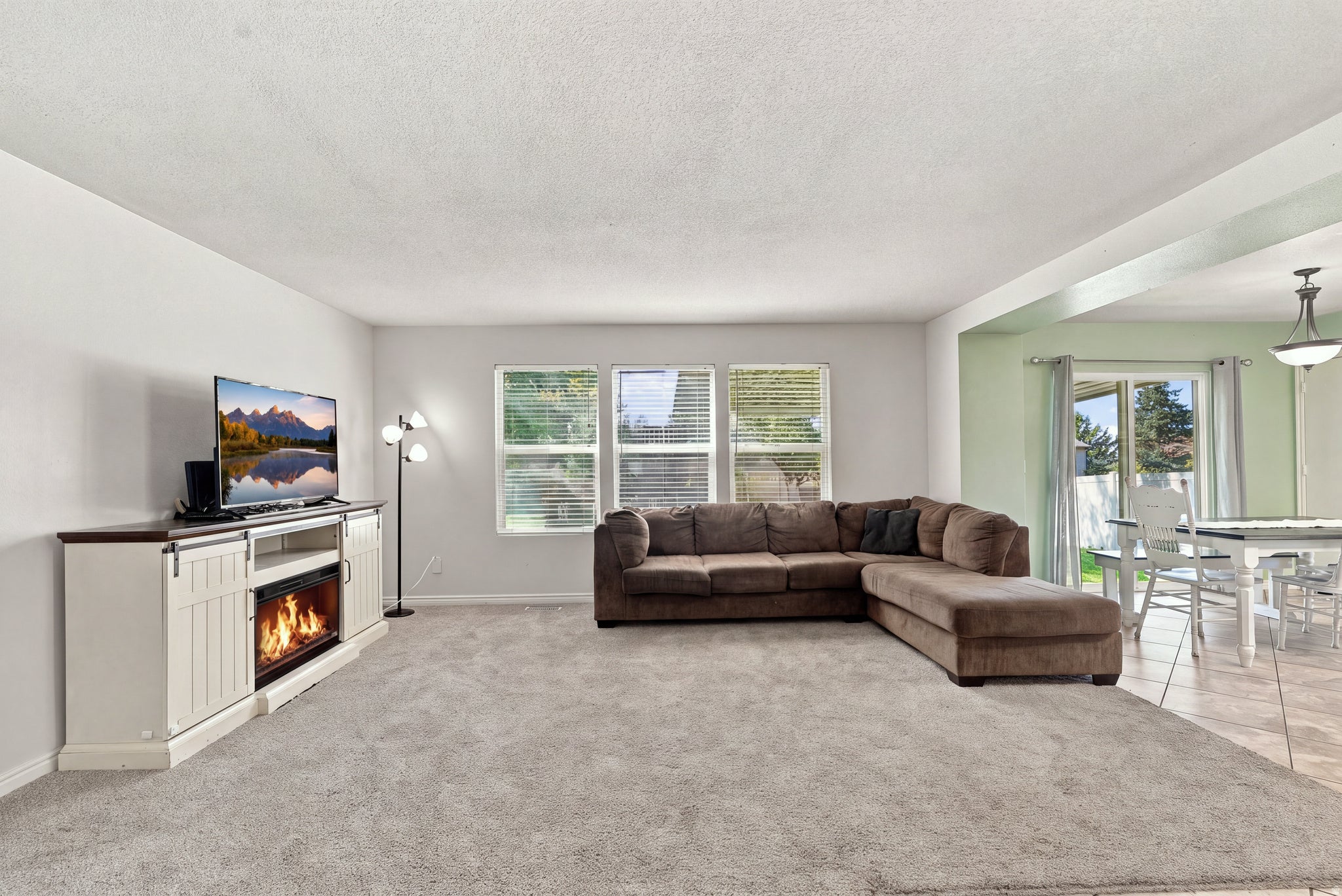 Spacious living area featuring light gray wall paint, light gray carpeting, and multiple windows