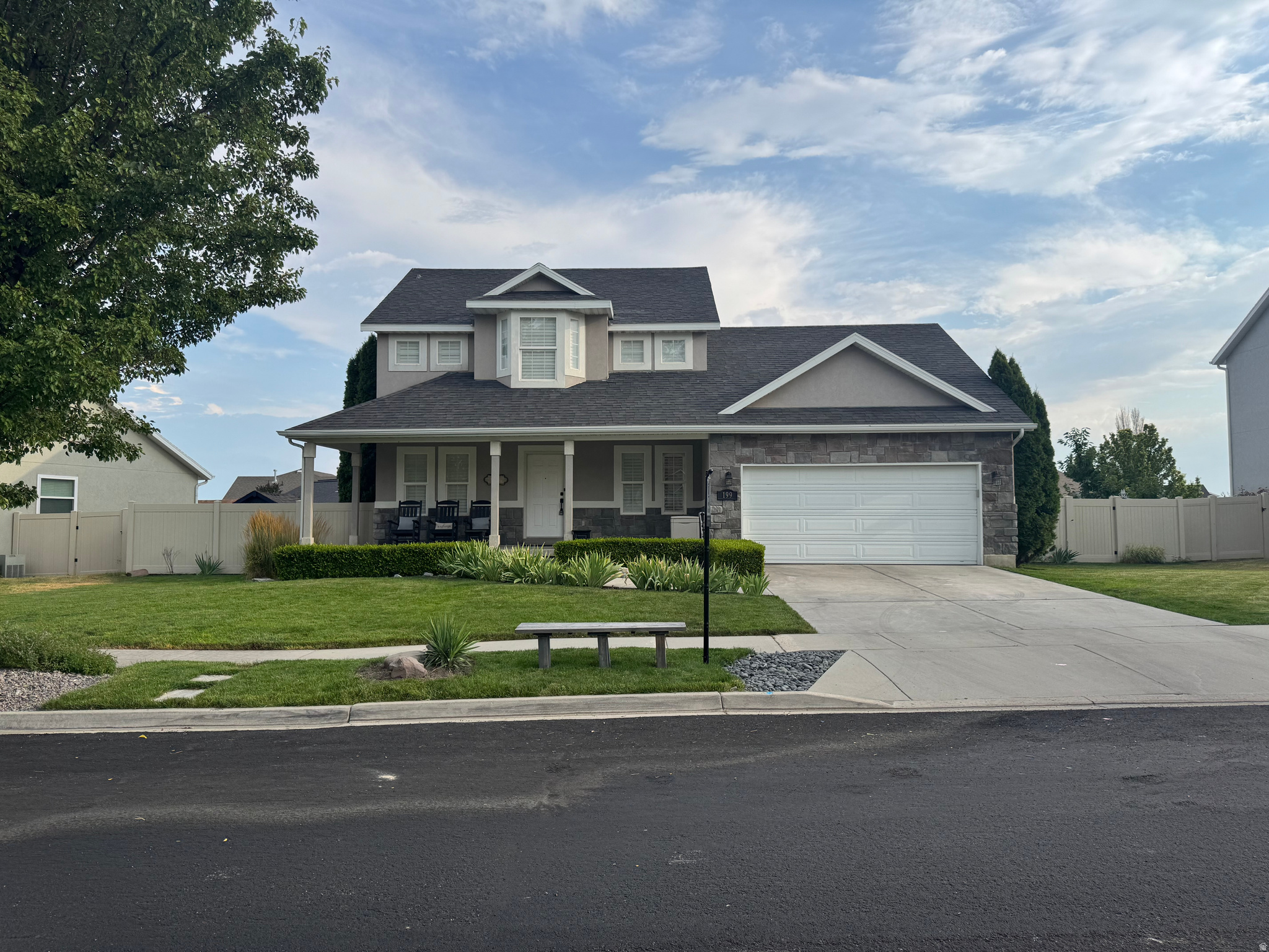 Two-story residence featuring a covered front porch with white columns, stone veneer accents, a two-car garage, and a concrete driveway
