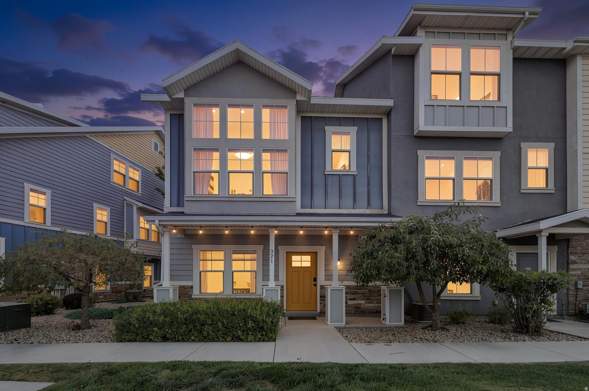 Contemporary multi-story exterior featuring a prominent front porch, a bright yellow entry door, and large windows on multiple levels