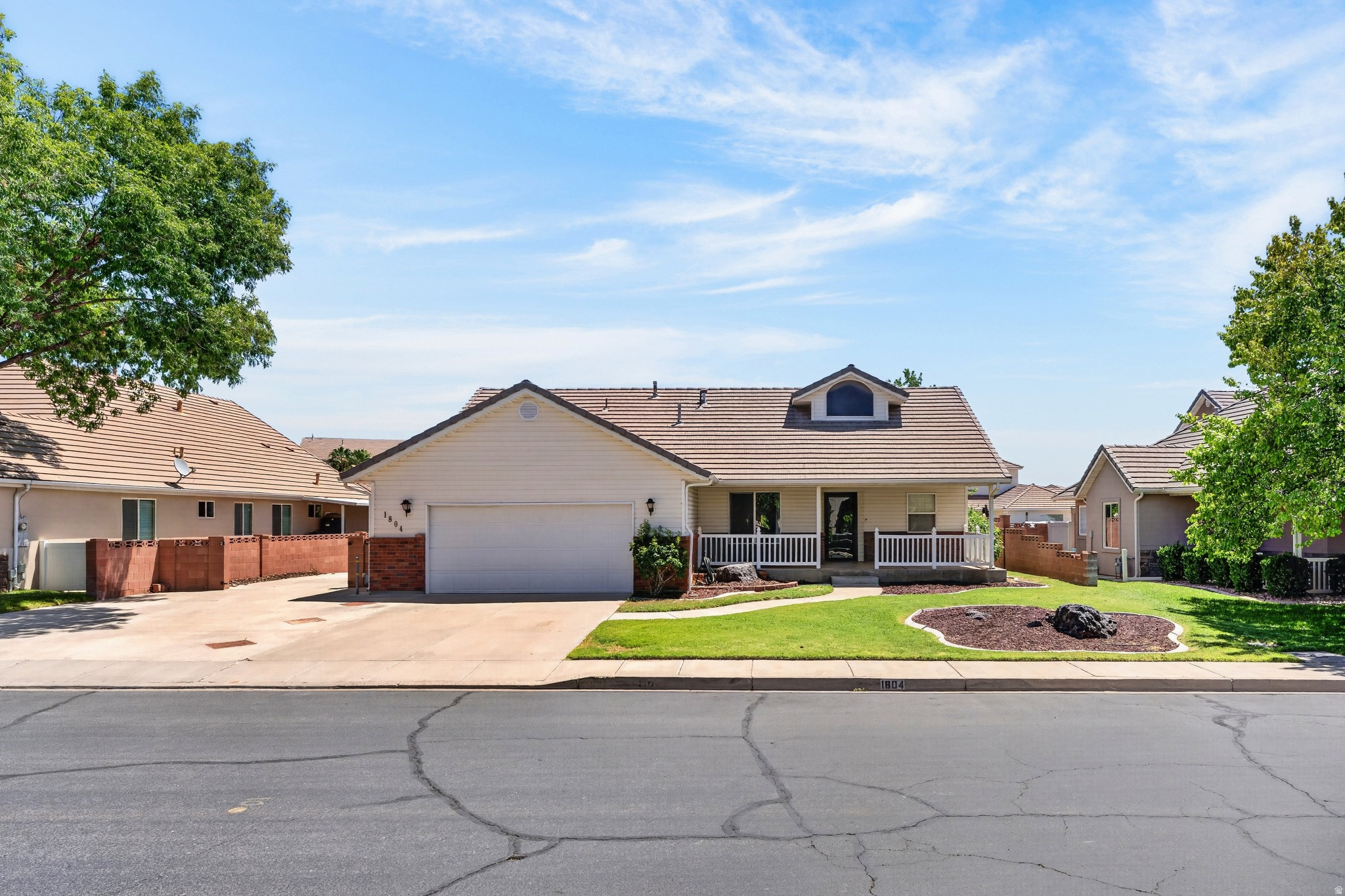 Traditional style residence featuring a covered front porch, an arched dormer window, a two-car garage, and a tiled roof