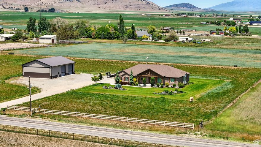 Welcome to this beautiful rustic country estate in the quaint town of Portage, Utah. Nestled on over 6 acres and surrounded by sweeping valley views and mountains, this 4656 sq. ft. ranch-style rambler was built with quality, comfort, and timeless design in mind. Inside, you'll find 4 spacious bedrooms, 4 bathrooms, and main-level living with an open floor plan featuring vaulted ceilings, wood flooring throughout, and three cozy gas fireplaces. The fully finished basement includes a private garage entrance, ideal for guests or extended family. A large laundry room with custom cabinetry and an oversized 3-car garage-equipped with hot/cold water and a utility sink-make everyday living both functional and convenient. Craftsmanship and efficiency were top priorities, with extra insulation, a whole-house ventilation system with heat exchanger, dual furnaces and water heaters, and two 1,000-gallon buried propane tanks. Both the home and the shop are supported by their own septic systems. Outdoor living is equally impressive. Relax on the covered patio with a gas fireplace, plumbed for a hot tub and perfect for summer picnics, while enjoying western sunsets and the property's 3-rail concrete fencing. A true standout is the 45x60 heated and fully insulated shop/airplane hangar-complete with a 40x14 hangar door, two 12x14 shop doors, 220 power, RV hookups, an indoor bathroom, and full exterior lighting. As an added opportunity, with a 2-acre minimum building requirement, the western pasture offers the potential to create an additional building lot with 200 ft. frontage (available only after the home has sold). This home has been immaculately cared for, built to last, and comes with TVs, state-of-the-art sound equipment, and a 12-month home warranty. Shown to qualified buyers by appointment only. Buyers to verify all information.