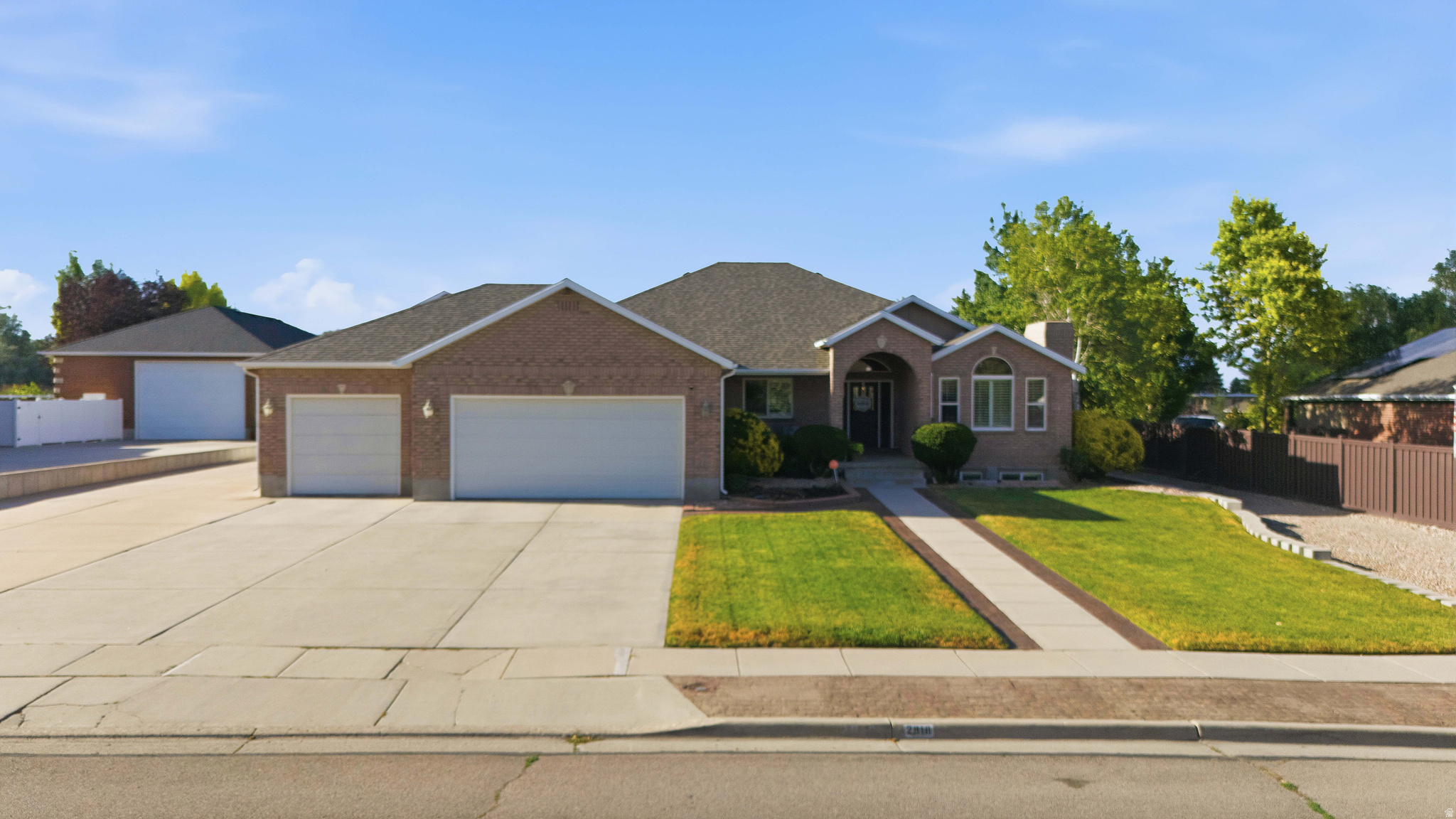 Brick exterior residence featuring a two-car garage, an additional detached garage with extended driveway, a landscaped front yard with mature trees, and a concrete pathway leading to the main entrance