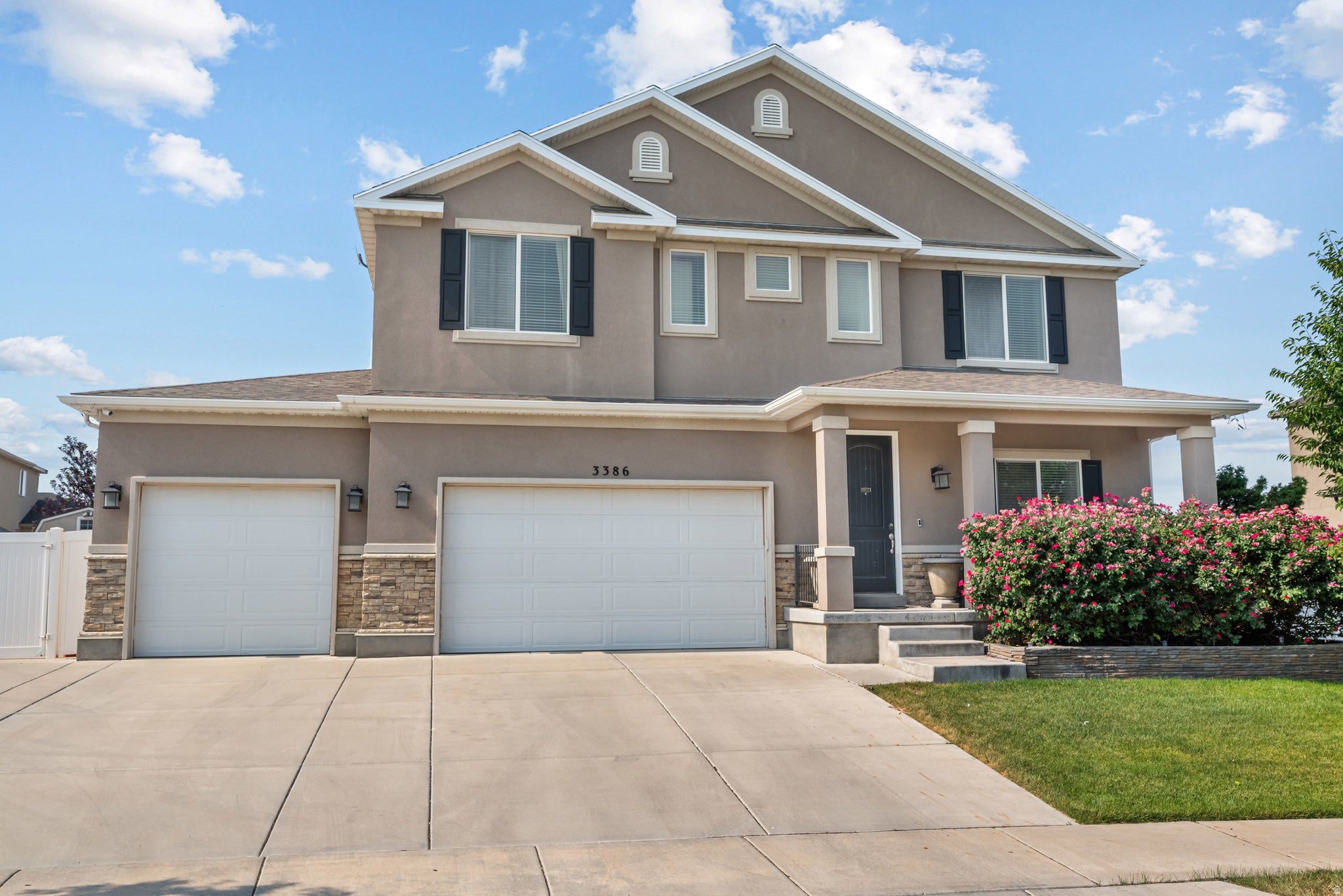 Two-story stucco exterior featuring a covered front porch, dual two-car garages with stone accents, and dark shutters
