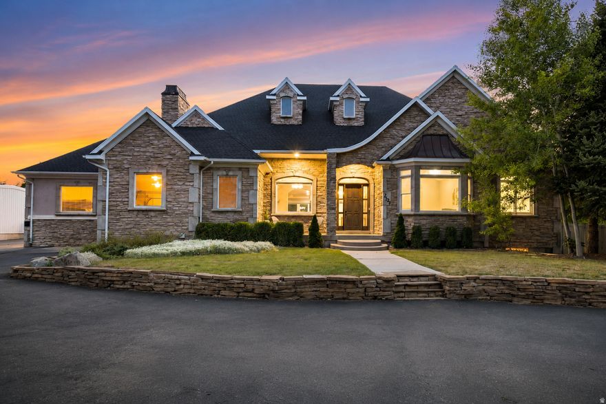 Open House: Saturday, May 16, 2026, from 10:00 AM to 2:00 PM. From the moment you turn down the private, tree-lined approach, this expansive stone-facade estate commands attention, admiration, and awe. This home invites you to picture your life there. Set on a spacious .64-acre lot in South Jordan, this 5-bedroom, 4.5-bath home offers 6,634 sq. ft. of living space, a 4-car garage, and additional exterior parking. From the warm stone exterior and mature landscaping to the welcoming front entry and beautiful evening curb appeal, the home immediately feels substantial, private, and special. Inside, the floor plan is designed for both everyday comfort and memorable gatherings. The main living areas feel bright and open, with large windows, high ceilings, detailed trim work, recessed lighting, and an easy flow between the kitchen, dining, and living spaces. The kitchen is a natural gathering place with white cabinetry, stainless steel appliances, quartz-style countertops, pendant lighting, a large island with bar seating, and a layout that keeps everyone connected. The home offers spaces for every season of life: quiet mornings in the dining room, relaxed evenings in the great room, movie nights in the theater room, game days in the finished basement, and summer nights outside under the covered patio. The primary suite provides a peaceful retreat with generous space, a tray ceiling, large windows, dual vanities, a soaking tub, separate shower, and excellent closet space. The fully finished basement adds exceptional flexibility with 3 bedrooms, 2 bathrooms, a large recreation/game area, theater room, and kitchenette-style space. It is ideal for entertaining, guests, extended living, or potential rental flexibility, subject to buyer verification and local requirements. Outdoors, the covered patio/deck areas, ceiling fans, mature trees, lawn space, and private-feeling backyard create the kind of setting buyers hope to find but rarely do. With its rare combination of scale, parking, finished basement space, indoor entertainment areas, outdoor living, and South Jordan location, this property is more than a home, it is a place to gather, grow, host, relax, and make memories. Set up an appointment now to see this beautiful home before you make any final decisions on a home, Buyers to verify all the information provided in this listing.