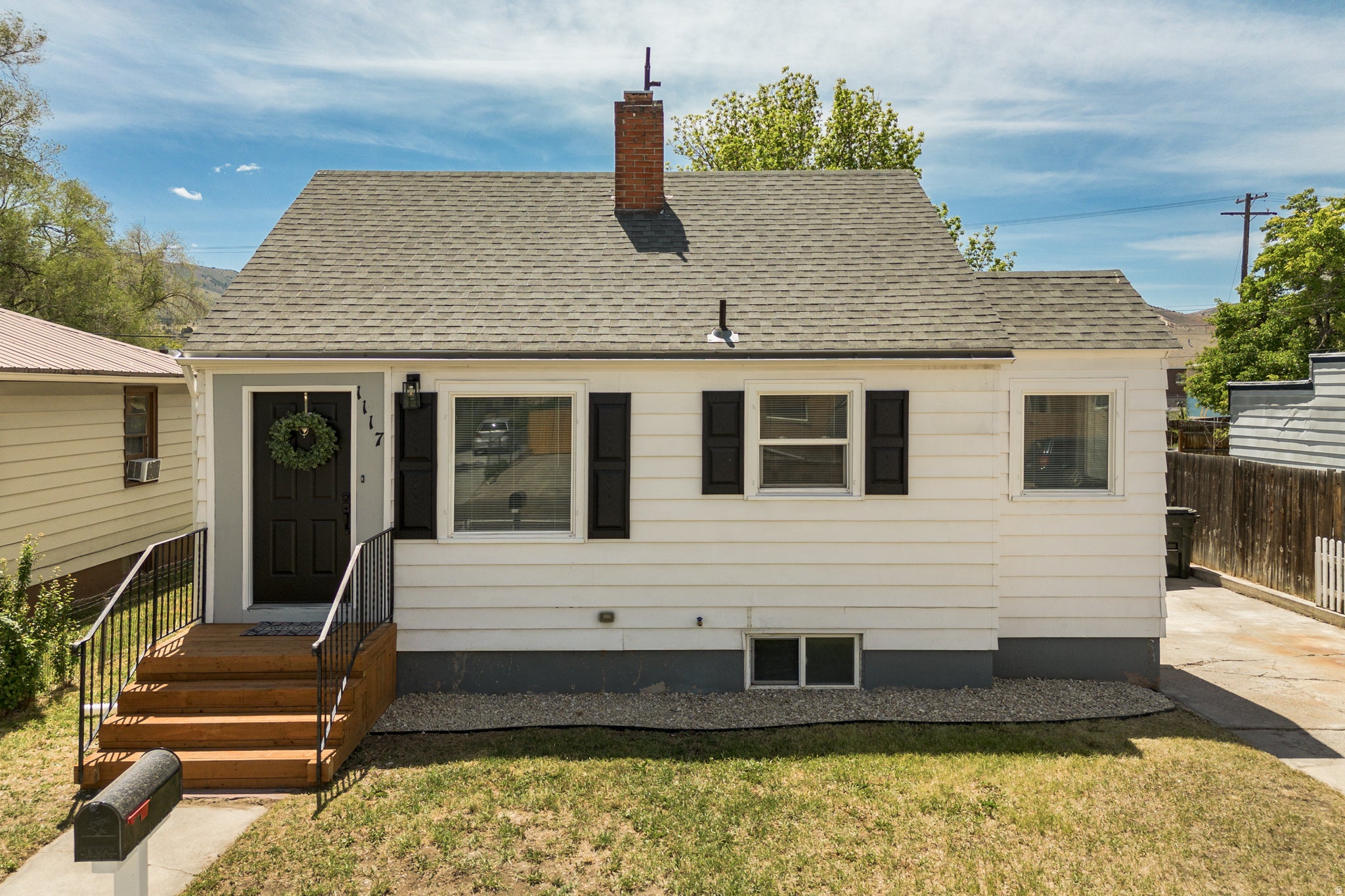 White siding exterior with a dark gray foundation, a gabled roof, and a red brick chimney