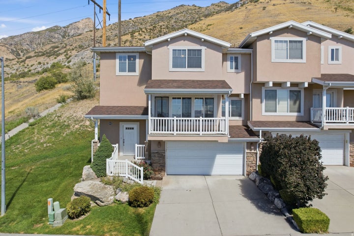Stucco exterior with gabled roof lines, multiple windows, an upper-level balcony, and an attached two-car garage