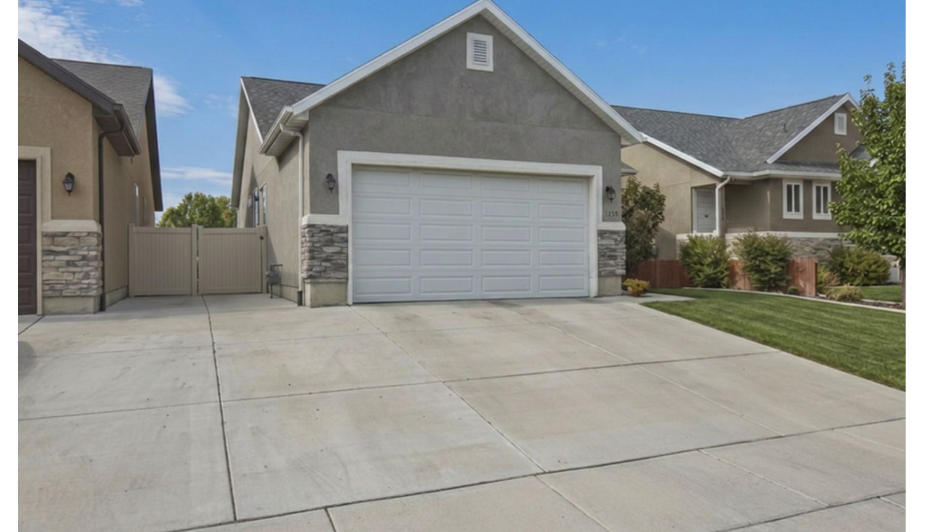 Stucco home featuring a two-car garage, stone accents, concrete driveway, and a fenced side yard