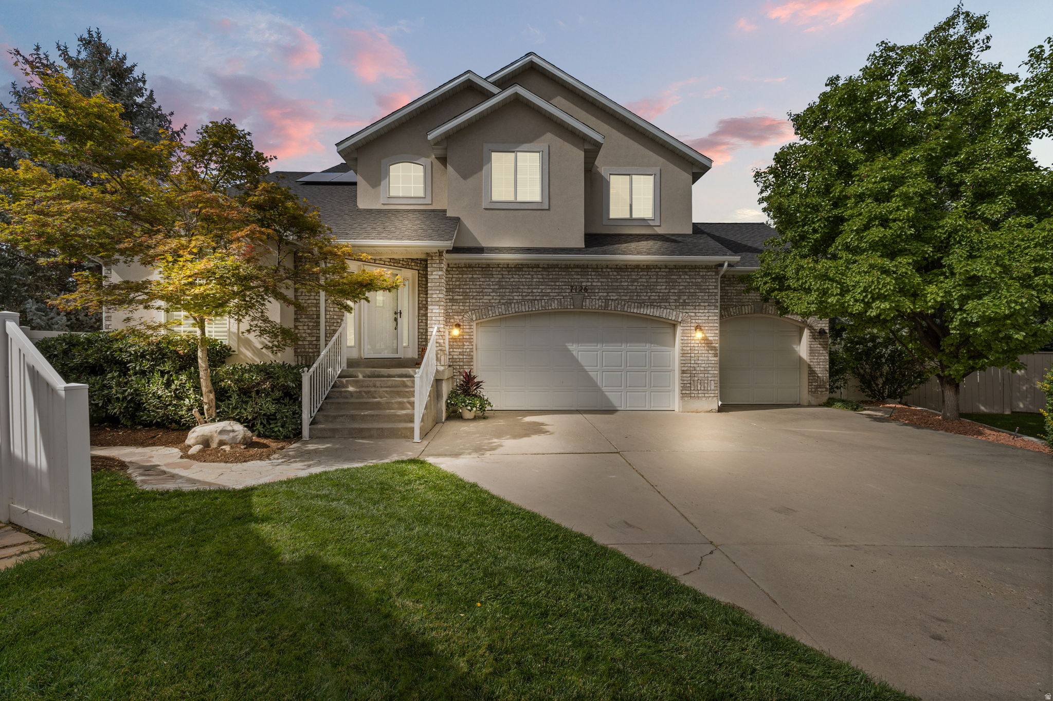 Traditional-style house with brick siding, concrete driveway, an attached garage, solar panels, and stucco siding