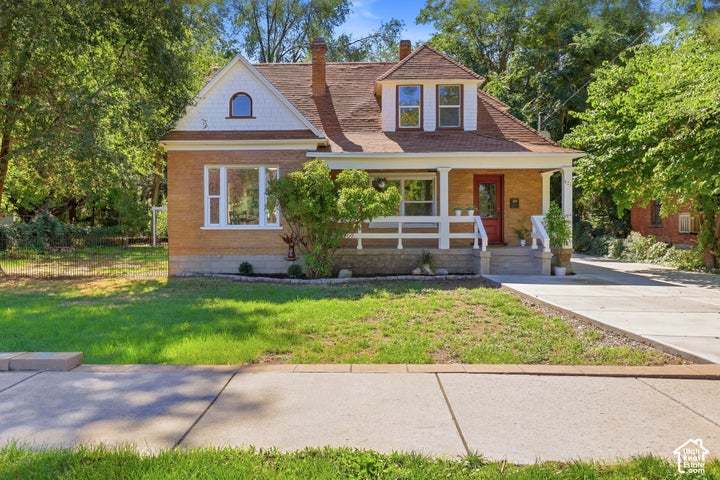 Brick exterior with white trim, covered front porch, red entryway door, upper-level dormer window, and paved driveway