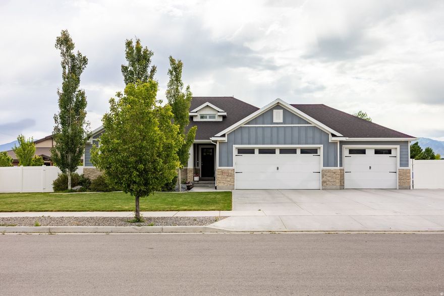 For those drawn to the idea of quieter streets, larger lots, and a home that feels established from day one, this Grantsville rambler offers a lifestyle that's becoming increasingly difficult to find near the Salt Lake Valley. Set on a fully fenced half-acre lot with mature landscaping, producing fruit trees, paved RV parking, irrigation water share, and no HOA, the property blends comfort, functionality, flexibility, and character with plenty of room to grow. Inside, soaring vaulted ceilings in the entryway make an immediate impression, welcoming you into light-filled living spaces with warm LVP flooring, a wood beam accent, and an open-concept layout designed for everyday living and gathering alike. The kitchen serves as the heart of the home with granite countertops, an oversized island, floating shelves, and a reclaimed wood pantry door, while shiplap accents, wood paneling, custom tilework, and shutters add warmth and personality throughout. Designed for easy main-level living, the home features a private primary suite filled with natural light, main-level laundry, and six spacious bedrooms with three bathrooms total, offering flexibility for guests, hobbies, work-from-home needs, or simply room to grow. The finished basement expands the living space with a projector and screen for the perfect home theater setup, a dry bar area, and a large storage room. Outside, the fully landscaped yard, mature trees, pergola, gas firepit, and established outdoor spaces create a move-in ready experience where the work has already been done and the home can be enjoyed from day one. A French door creates an effortless connection from the main living space to the backyard, while the irrigation water share adds practicality and long-term value for maintaining the lush landscaping with ease. If you find yourself craving a little more breathing room without giving up convenience, this home offers the balance of peaceful small-town living with an easy commute back to the Salt Lake Valley, all within a property that feels established, inviting, and ready to enjoy from the moment you arrive.