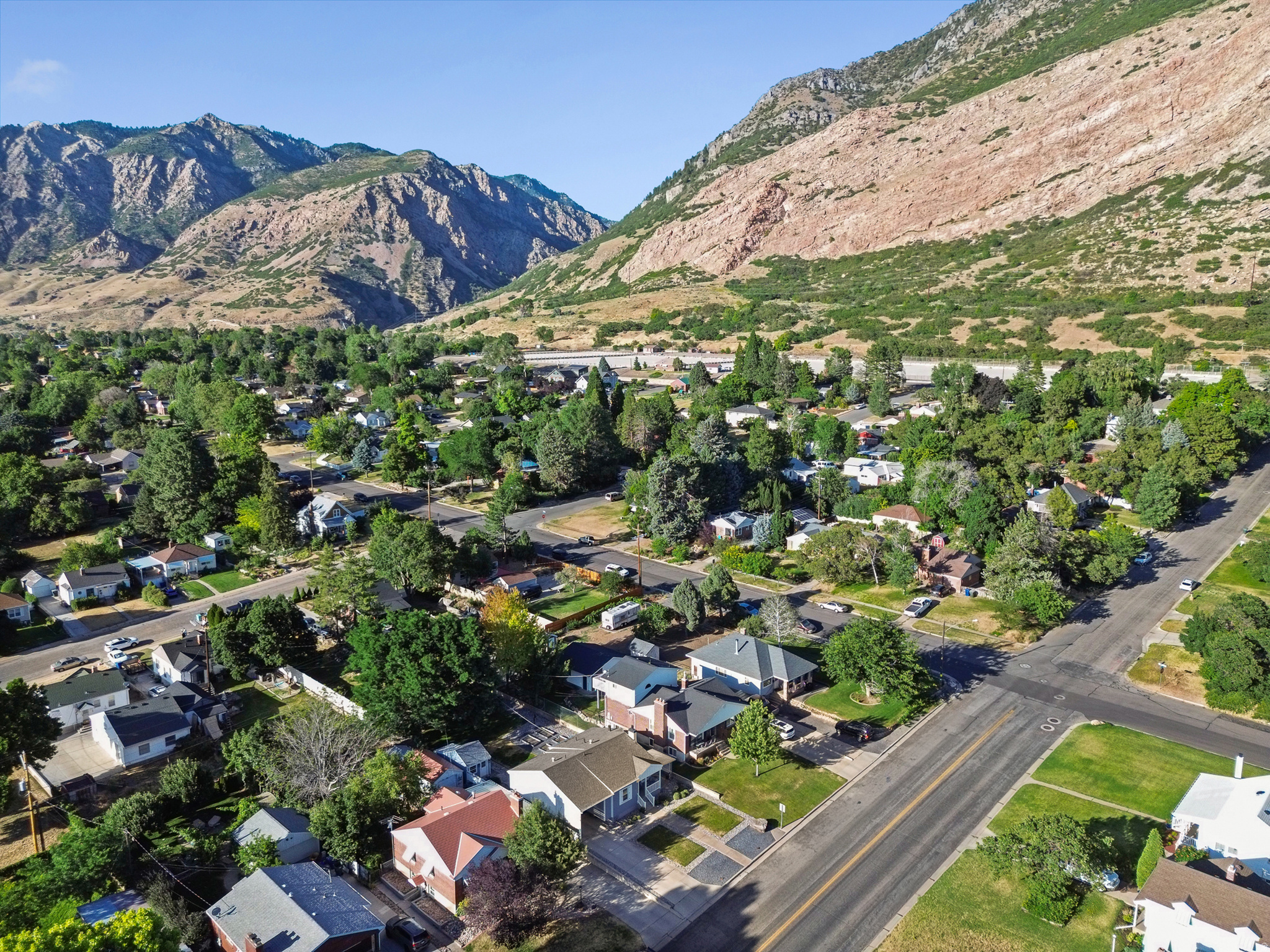 Aerial perspective showcasing a residential area with mature trees and paved streets, set against a backdrop of mountainous terrain